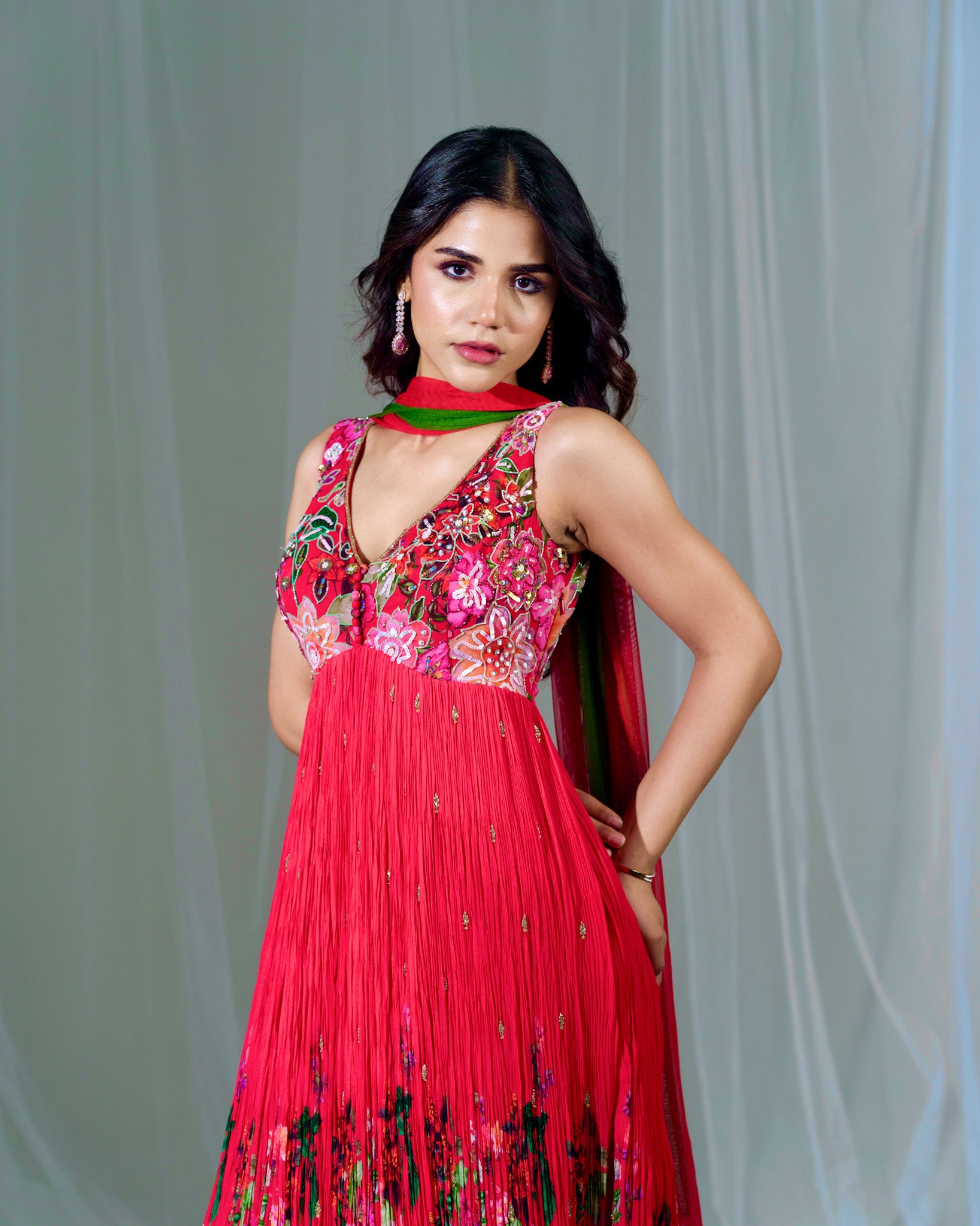 Woman wearing a red floral dress with a green scarf against a light gray background
