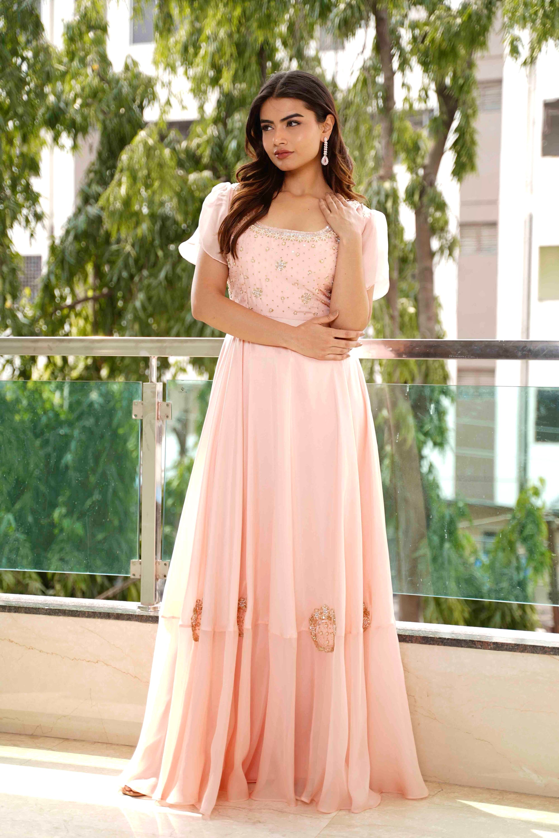 Woman in a pink dress standing on a balcony with greenery in the background