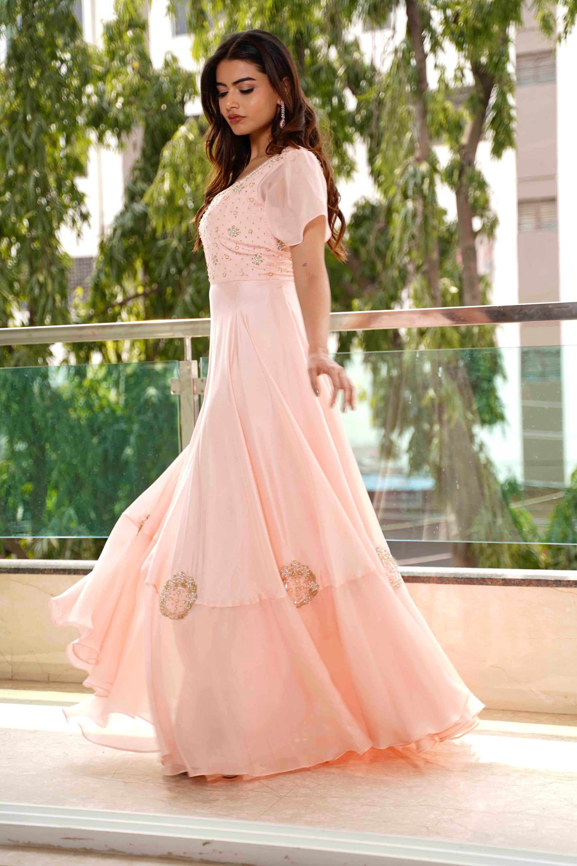 Woman in a peach evening gown standing on a balcony with greenery in the background