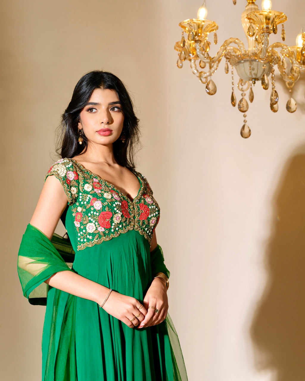 Woman in a green embroidered dress standing in front of a chandelier.