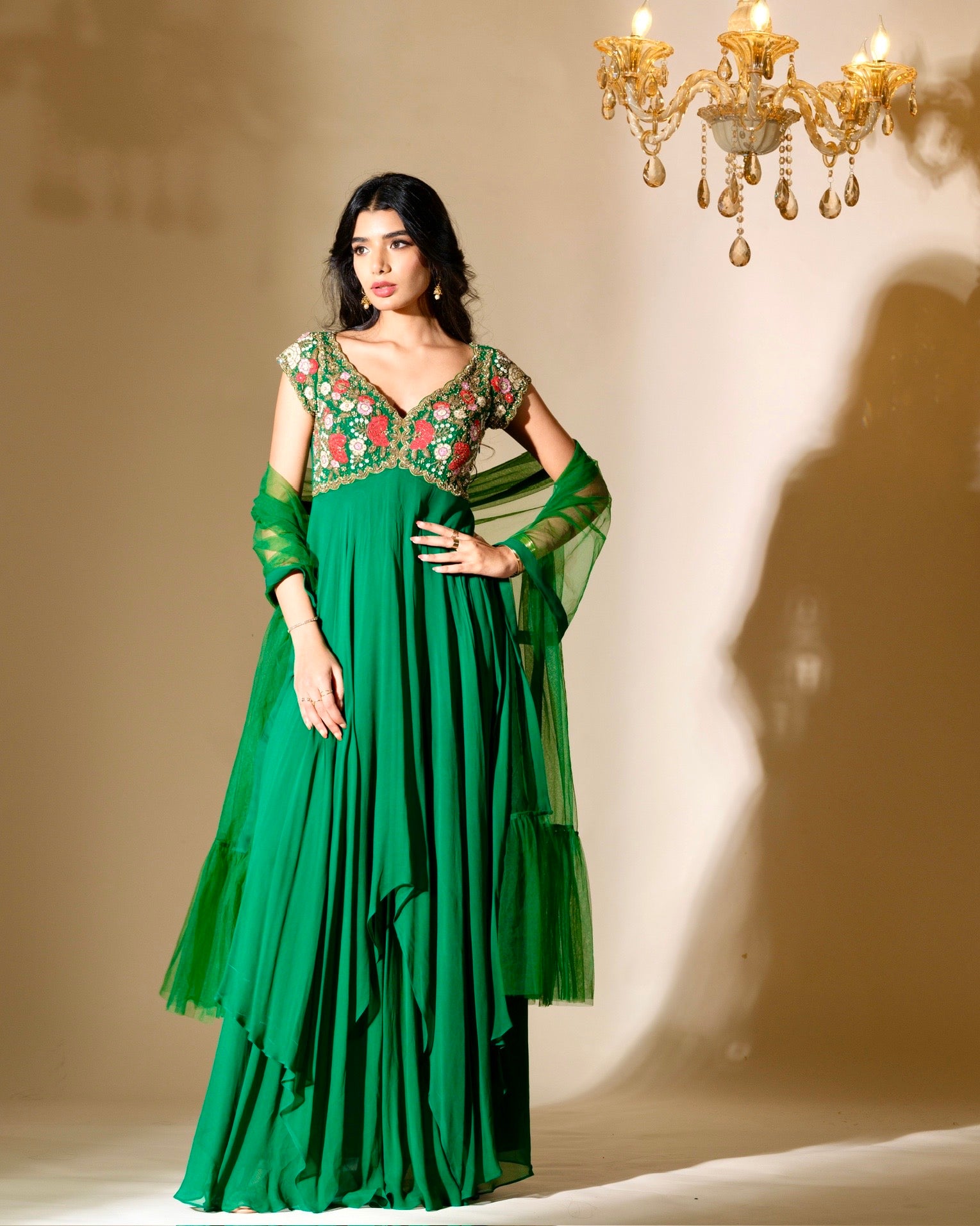 Woman wearing a green traditional outfit with floral embroidery in a dimly lit room.