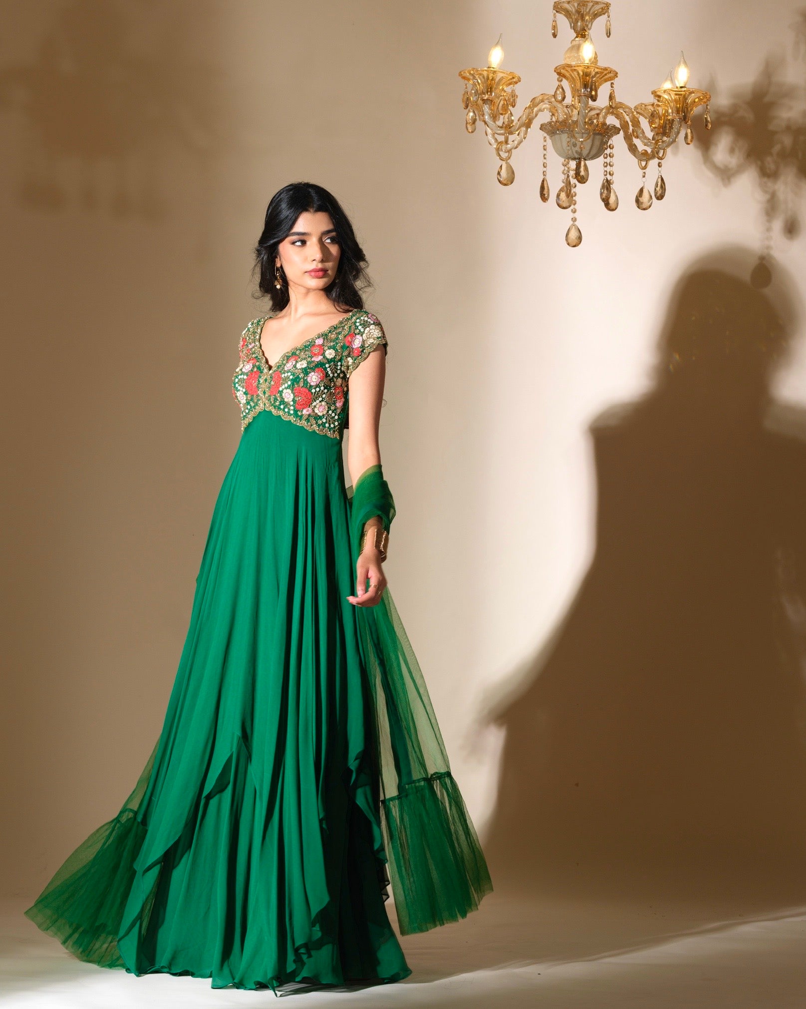 Woman in a green evening gown with floral embellishments standing in front of a chandelier.