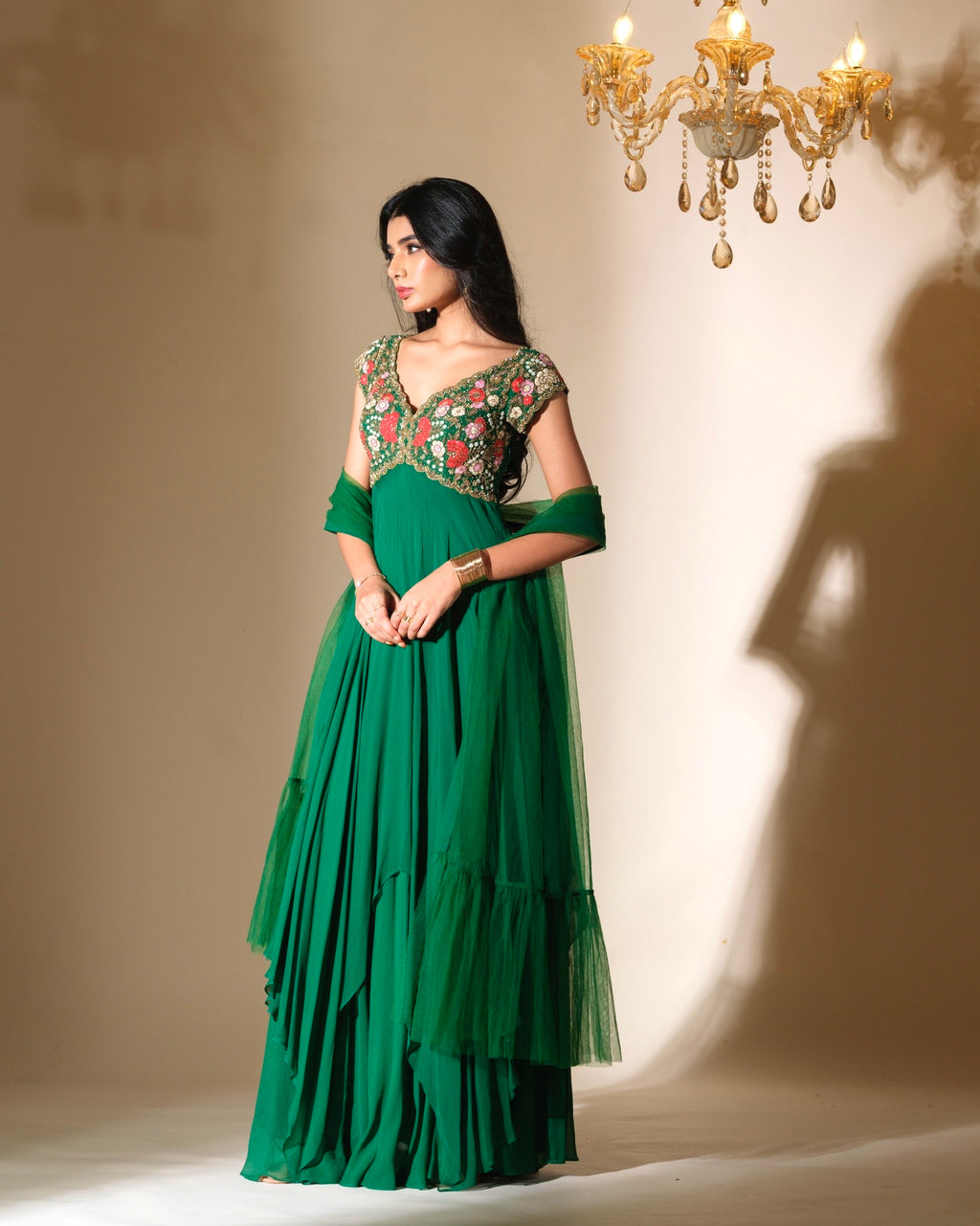 Woman wearing a green dress with floral embellishments in a softly lit room.