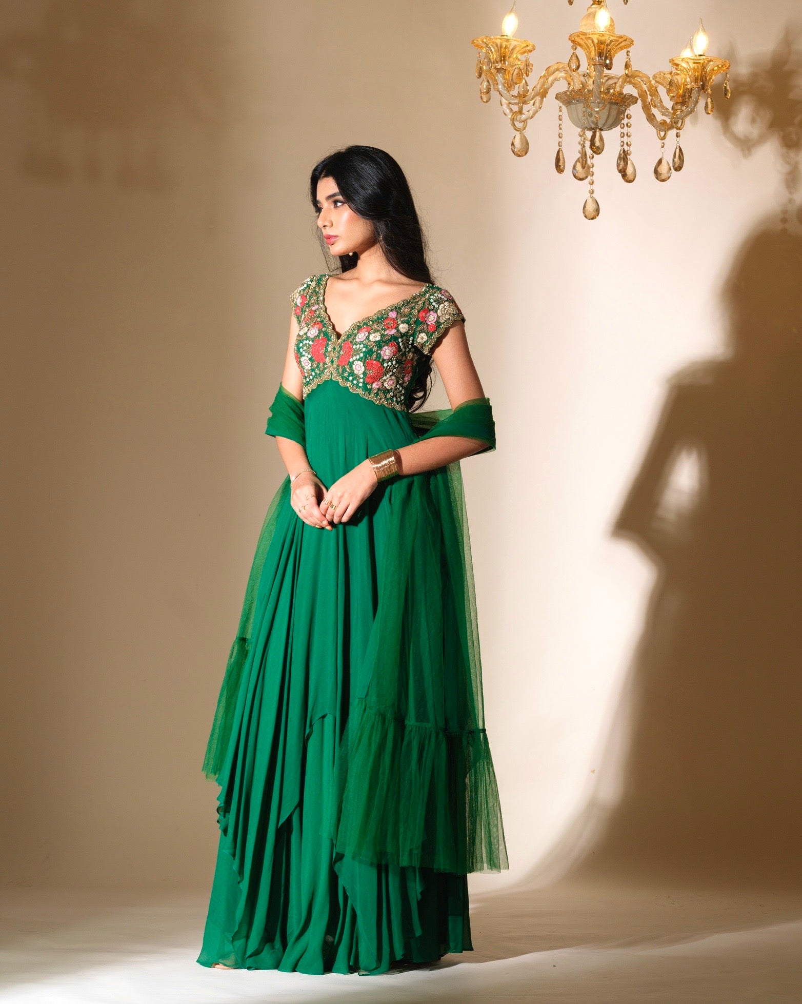 Woman wearing a green dress with floral embellishments in a softly lit room.