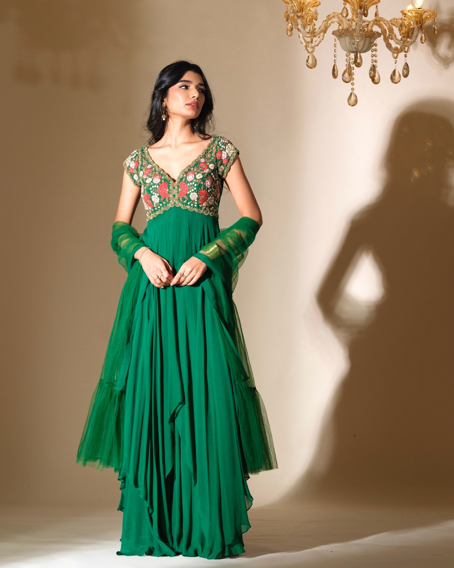 Woman wearing a green dress with floral embellishments in a warm-toned room.