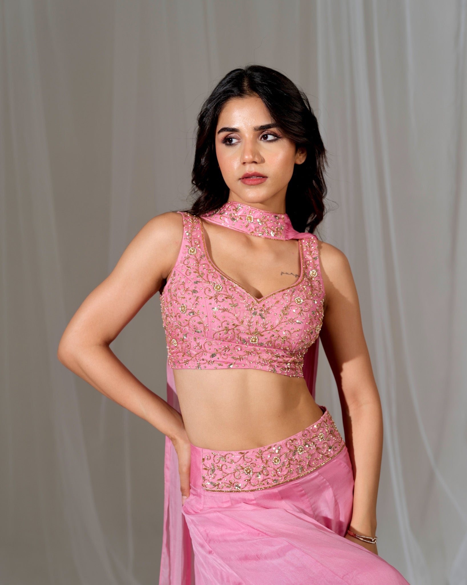 Woman wearing a pink embroidered traditional outfit against a plain background