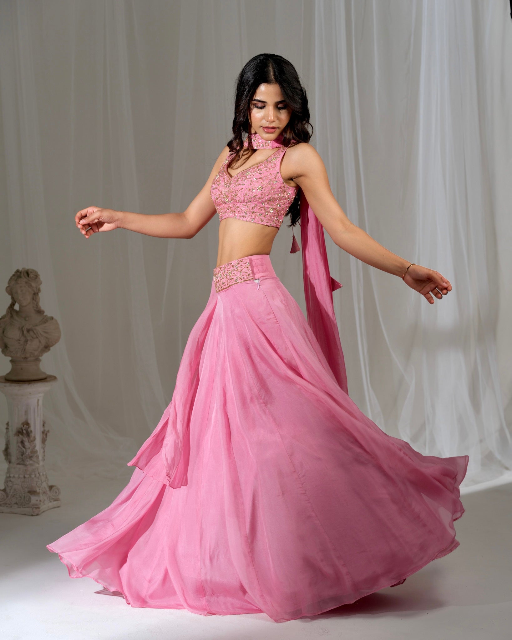 Woman in a pink traditional outfit with a flowing skirt against a neutral background