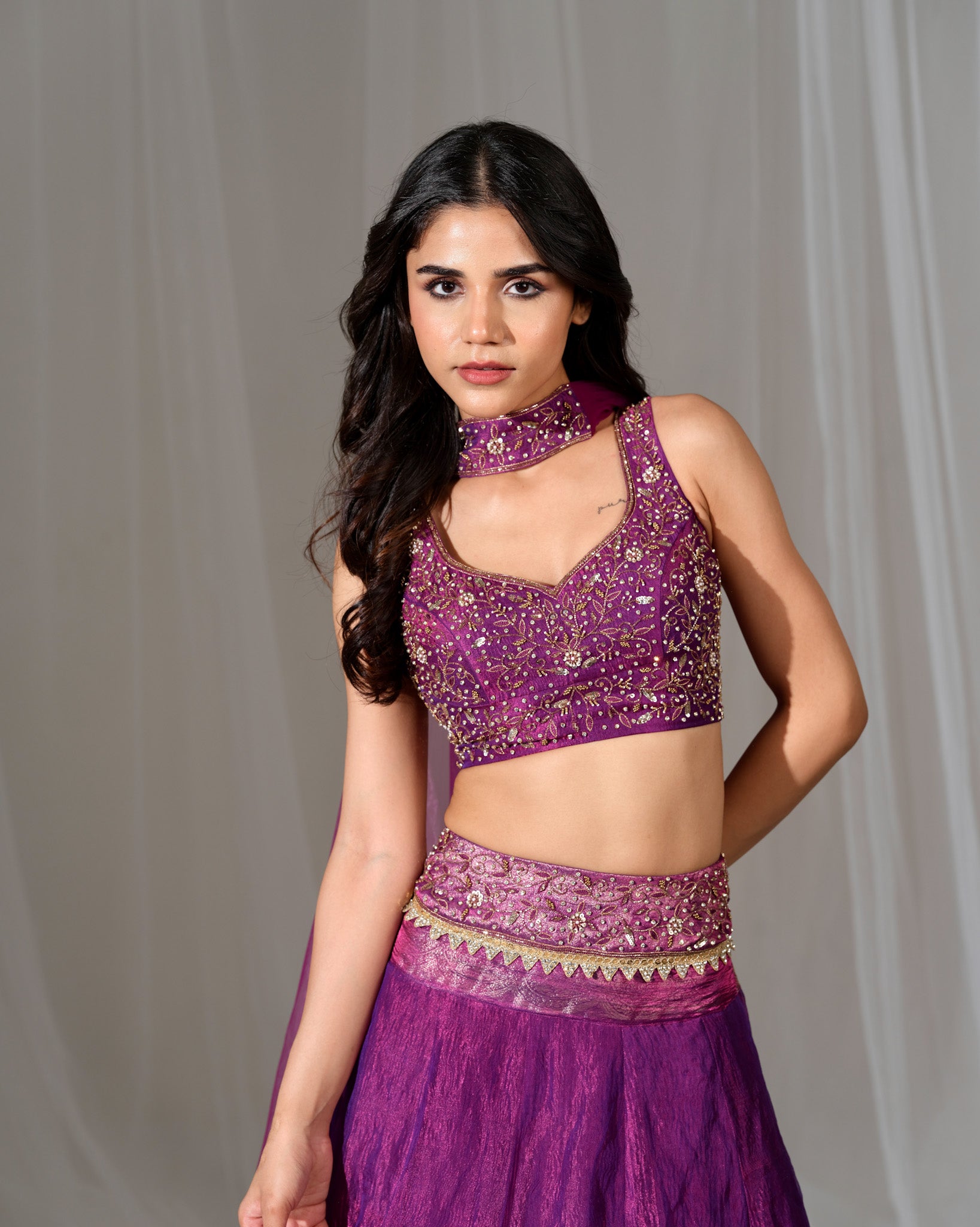 Woman wearing a purple traditional outfit with intricate designs against a plain background