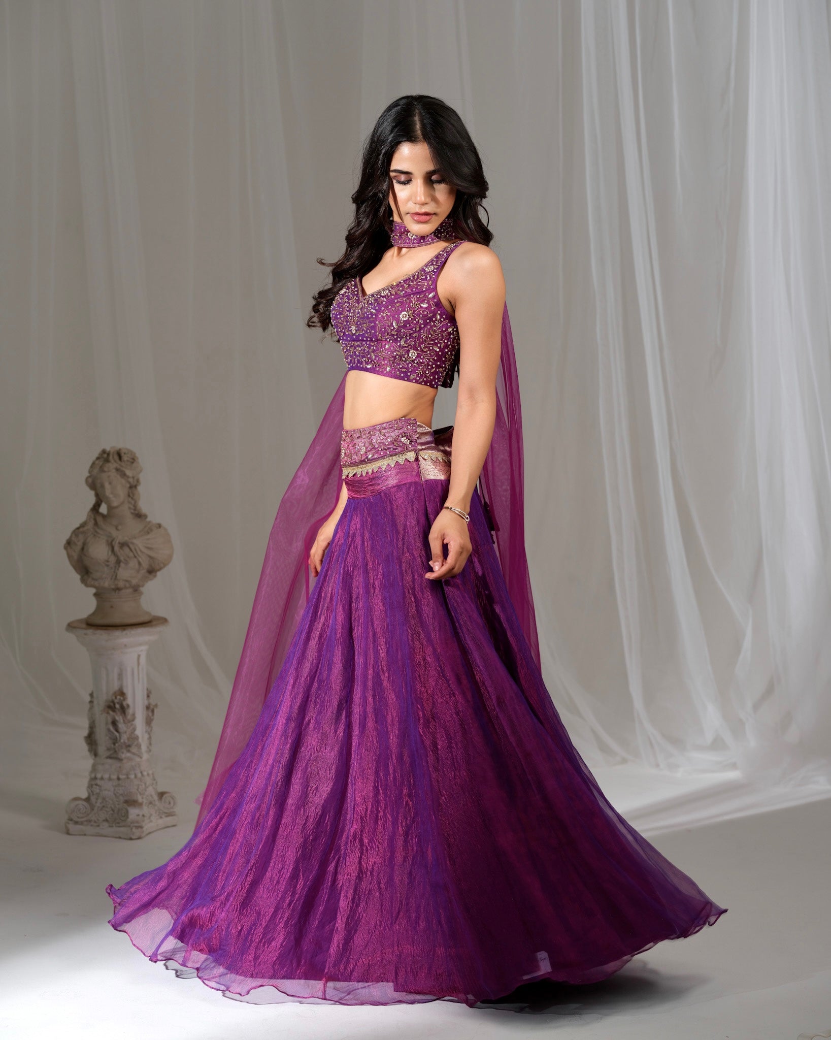 Woman wearing a purple traditional outfit with a matching cape against a gray background