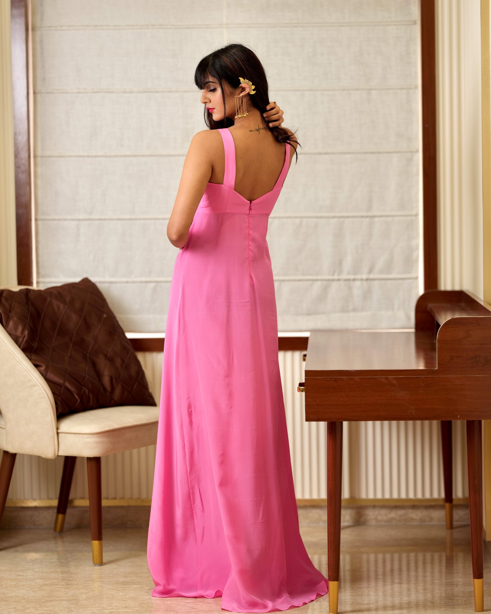 Woman in a pink dress standing in a room with a chair and table.