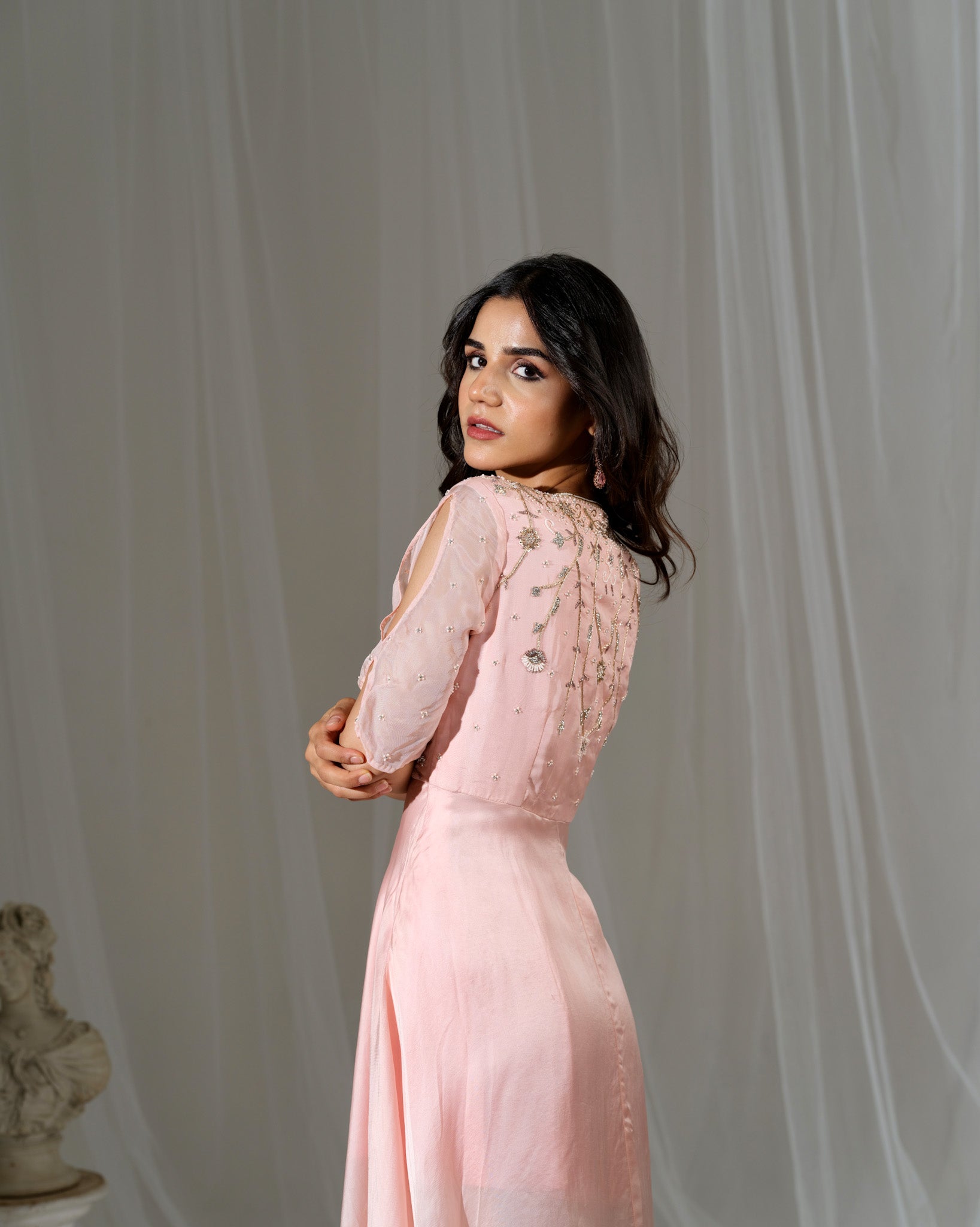 Woman in a pink dress standing against a white curtain