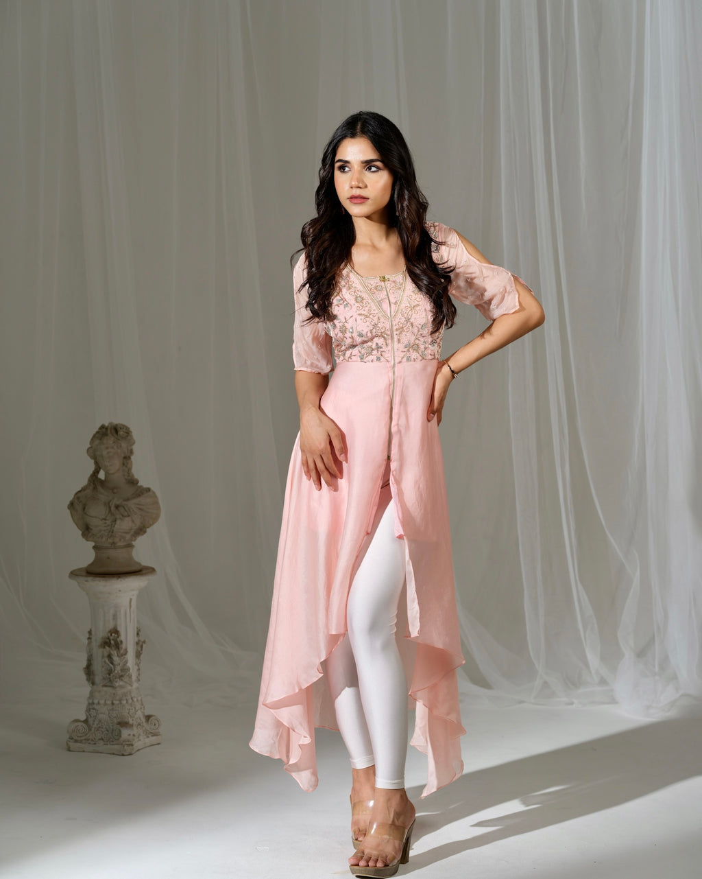 Woman wearing a pink outfit with white pants against a neutral background