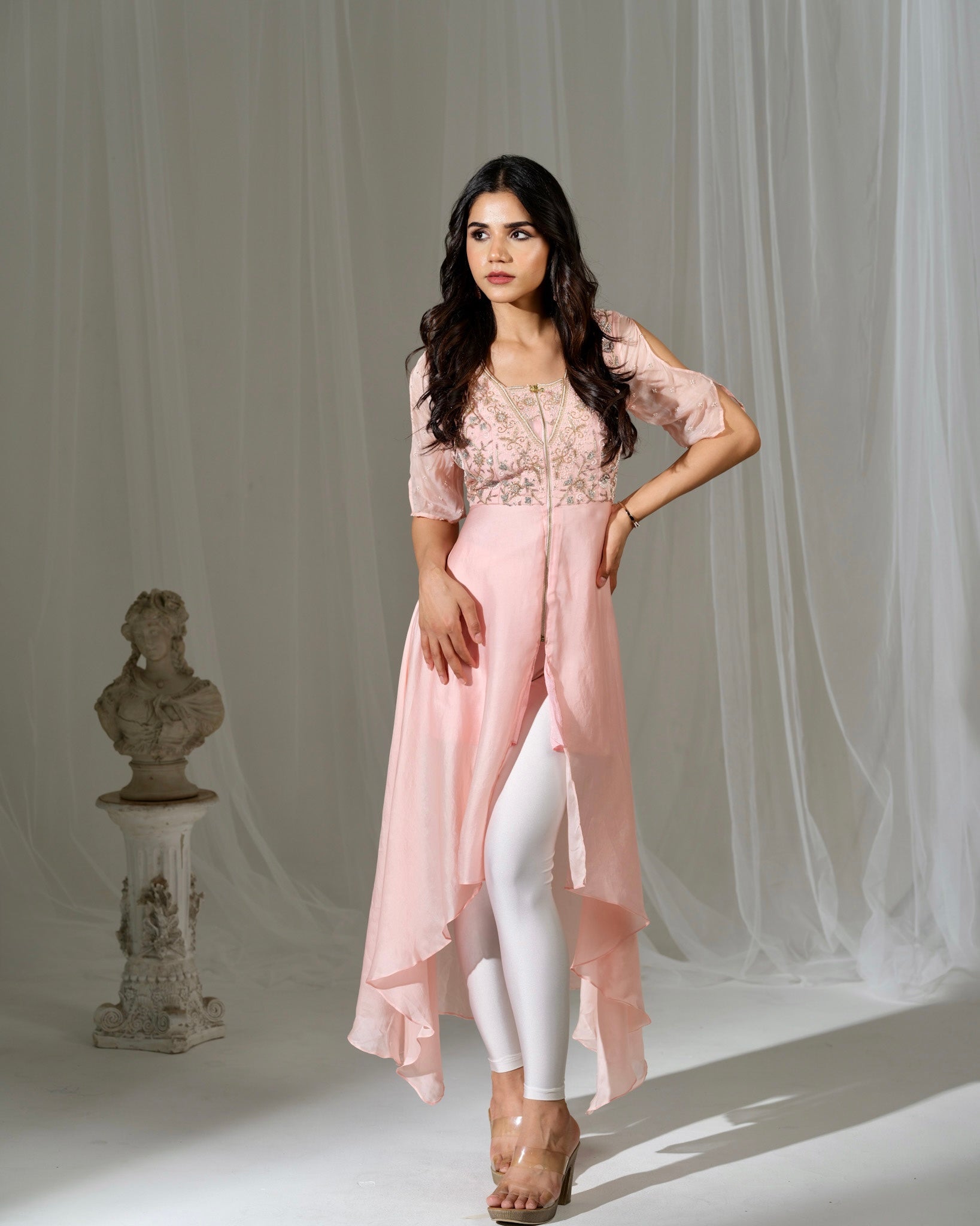 Woman wearing a pink outfit with white pants against a neutral background