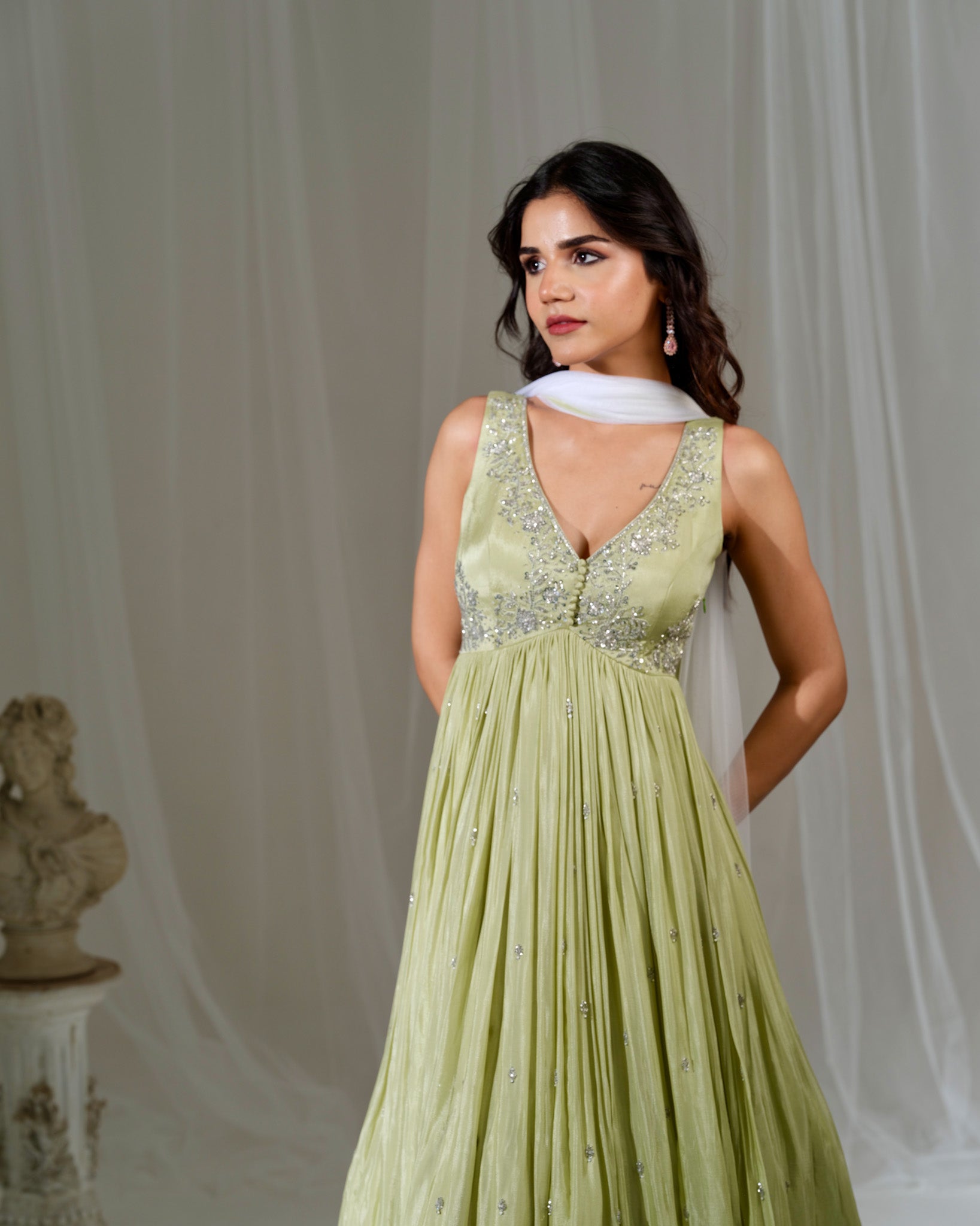 Woman wearing a light green evening gown with a white scarf in a studio setting