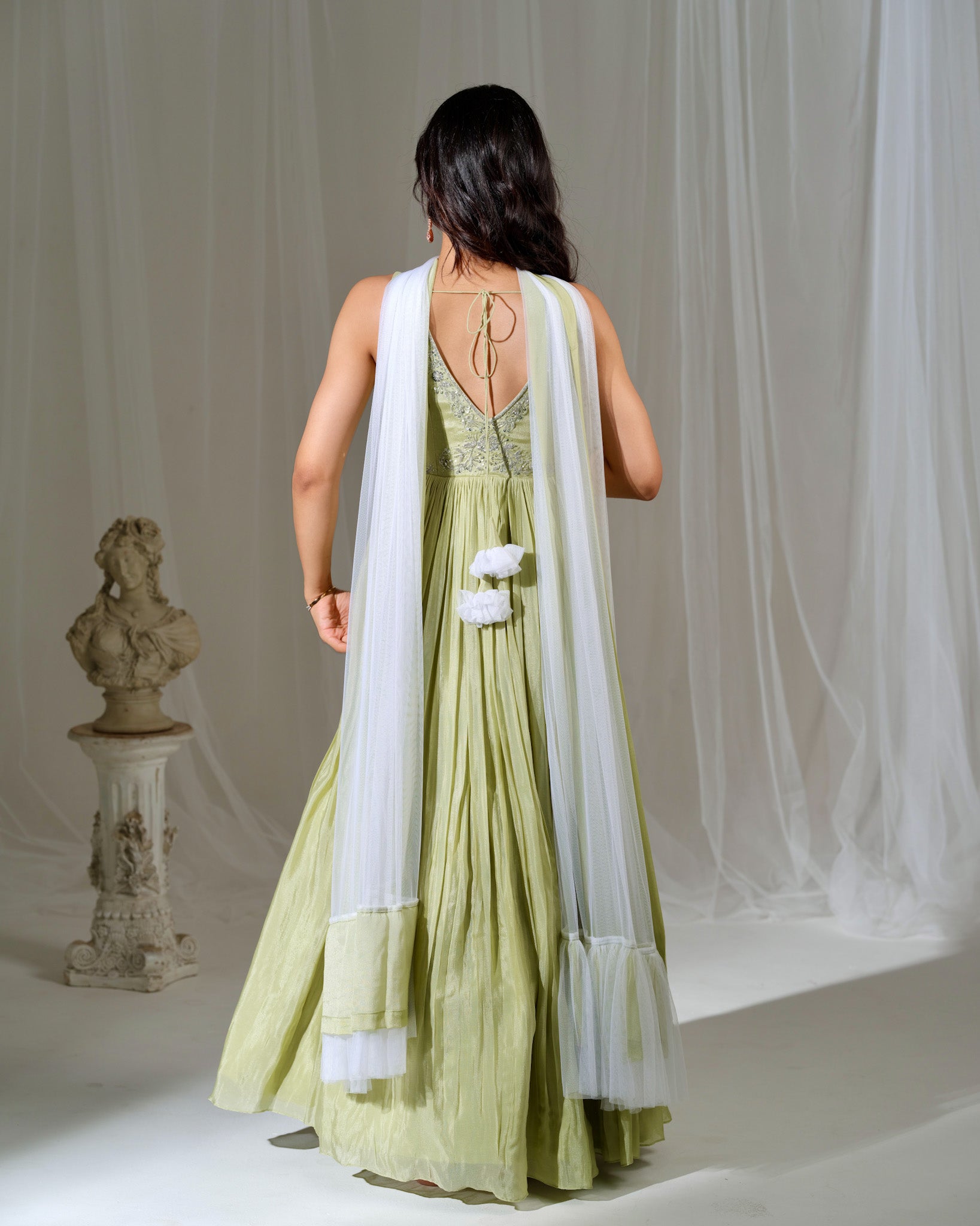 Woman in a green dress with a white dupatta standing in a softly lit room.