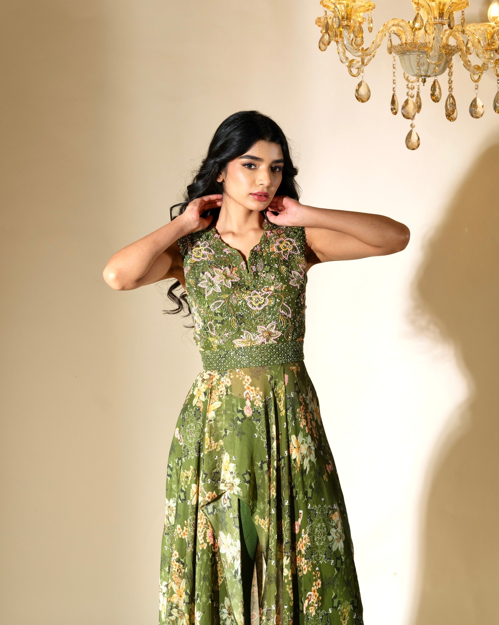 Woman wearing a green floral dress in an elegant indoor setting with a chandelier.