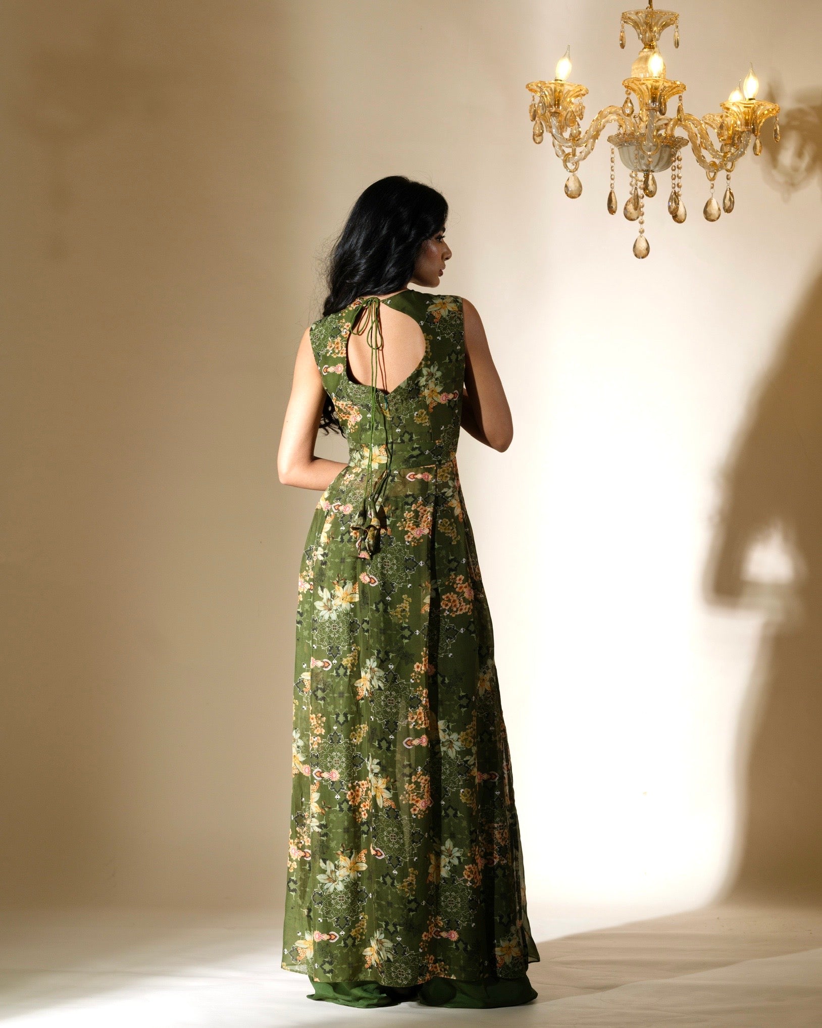 Woman in a green floral dress standing in a softly lit room with a chandelier.