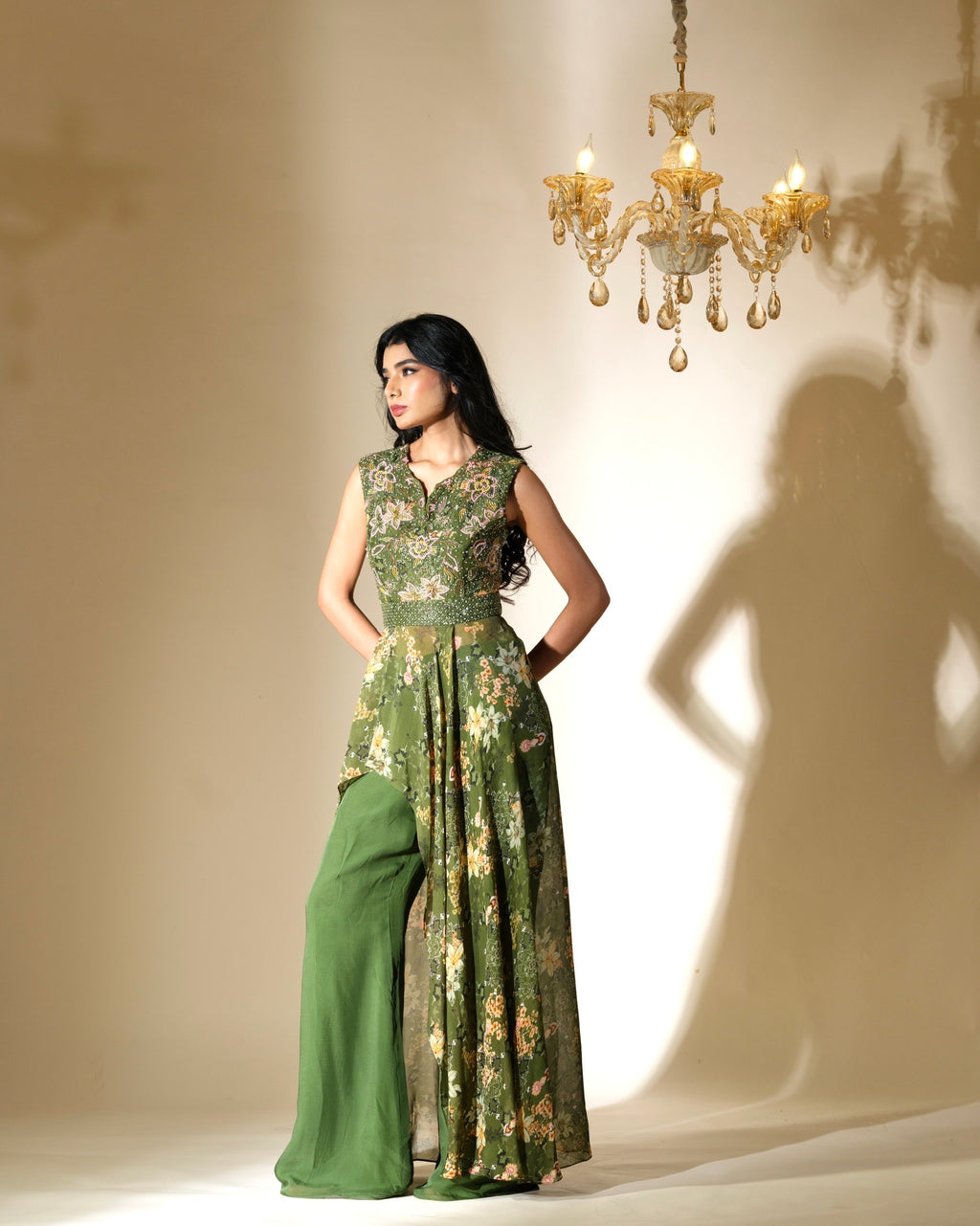 Woman wearing a green floral dress standing in front of a chandelier casting a shadow.