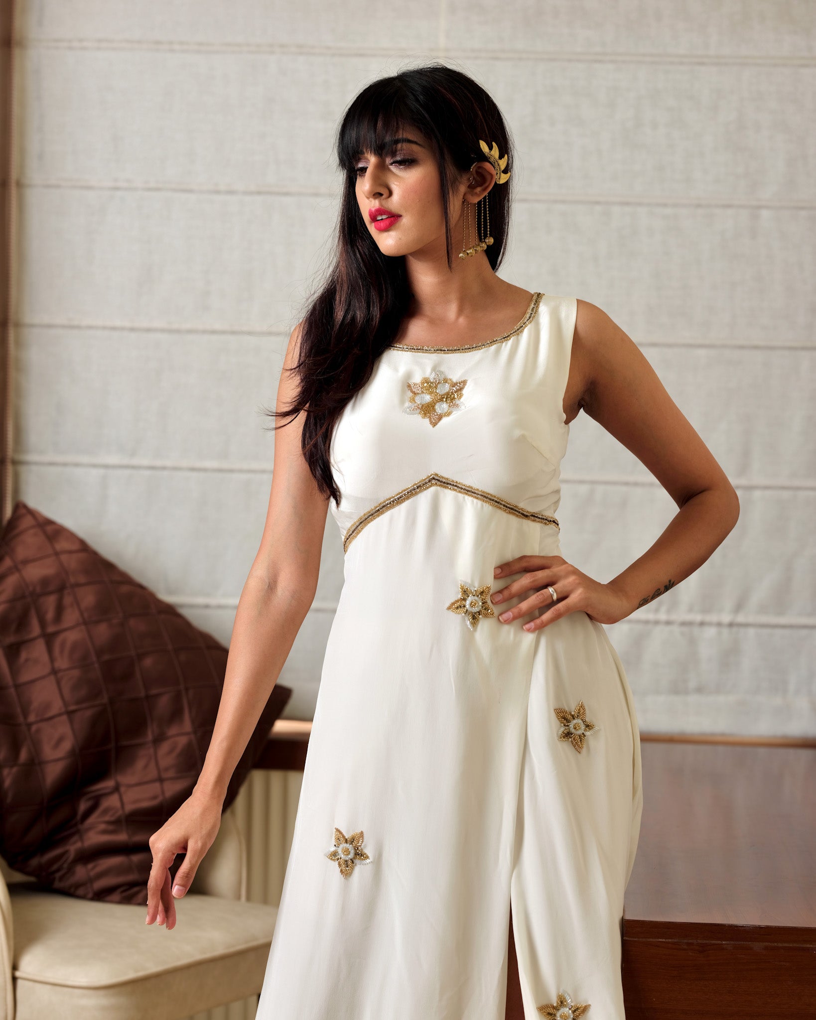 Woman wearing a white outfit with gold embellishments in an indoor setting.