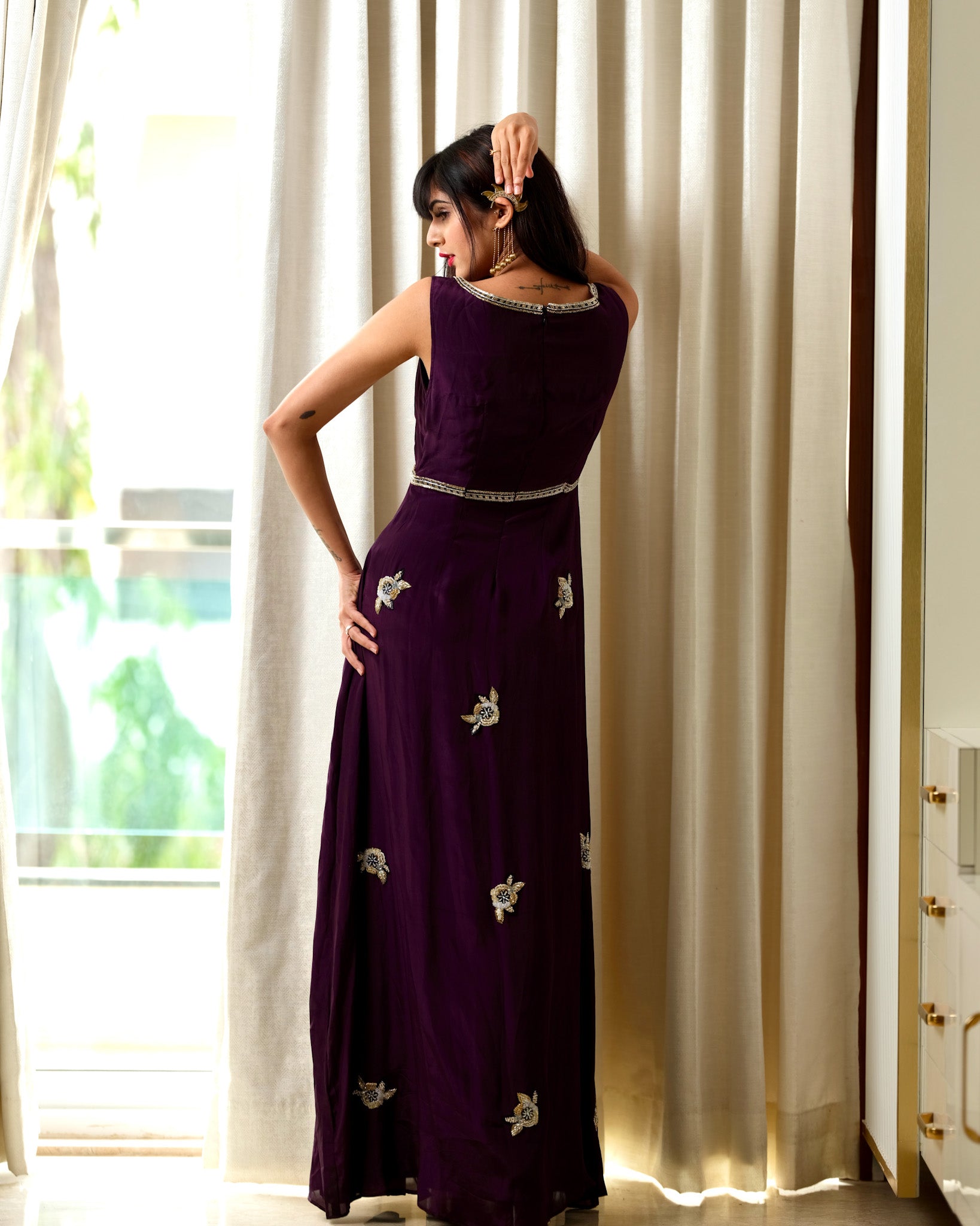 Woman wearing a purple dress with silver embellishments in a bright room.
