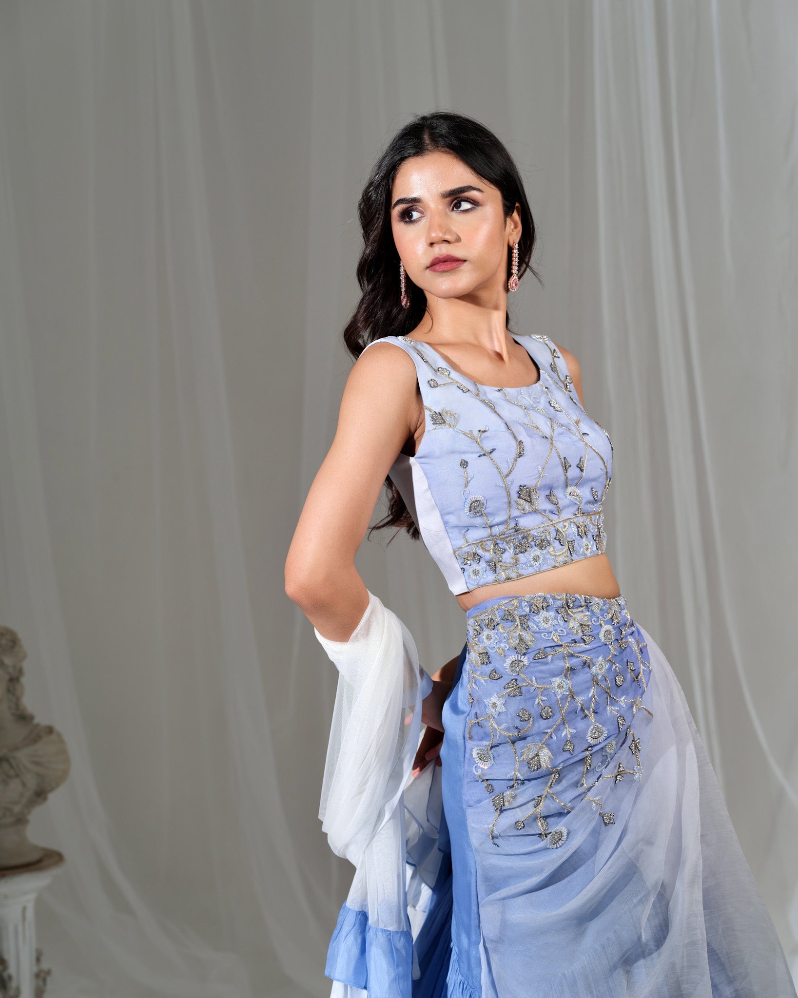 Woman wearing a light blue traditional outfit with intricate designs against a gray background