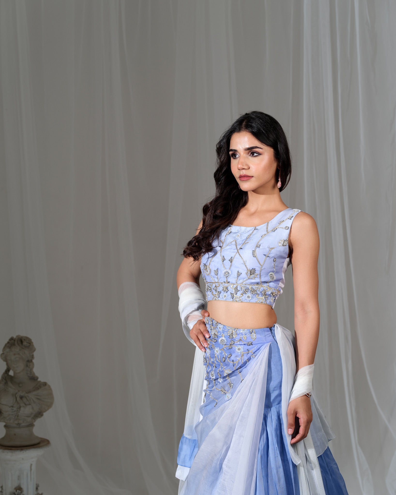 Woman wearing a light blue embroidered outfit against a gray background