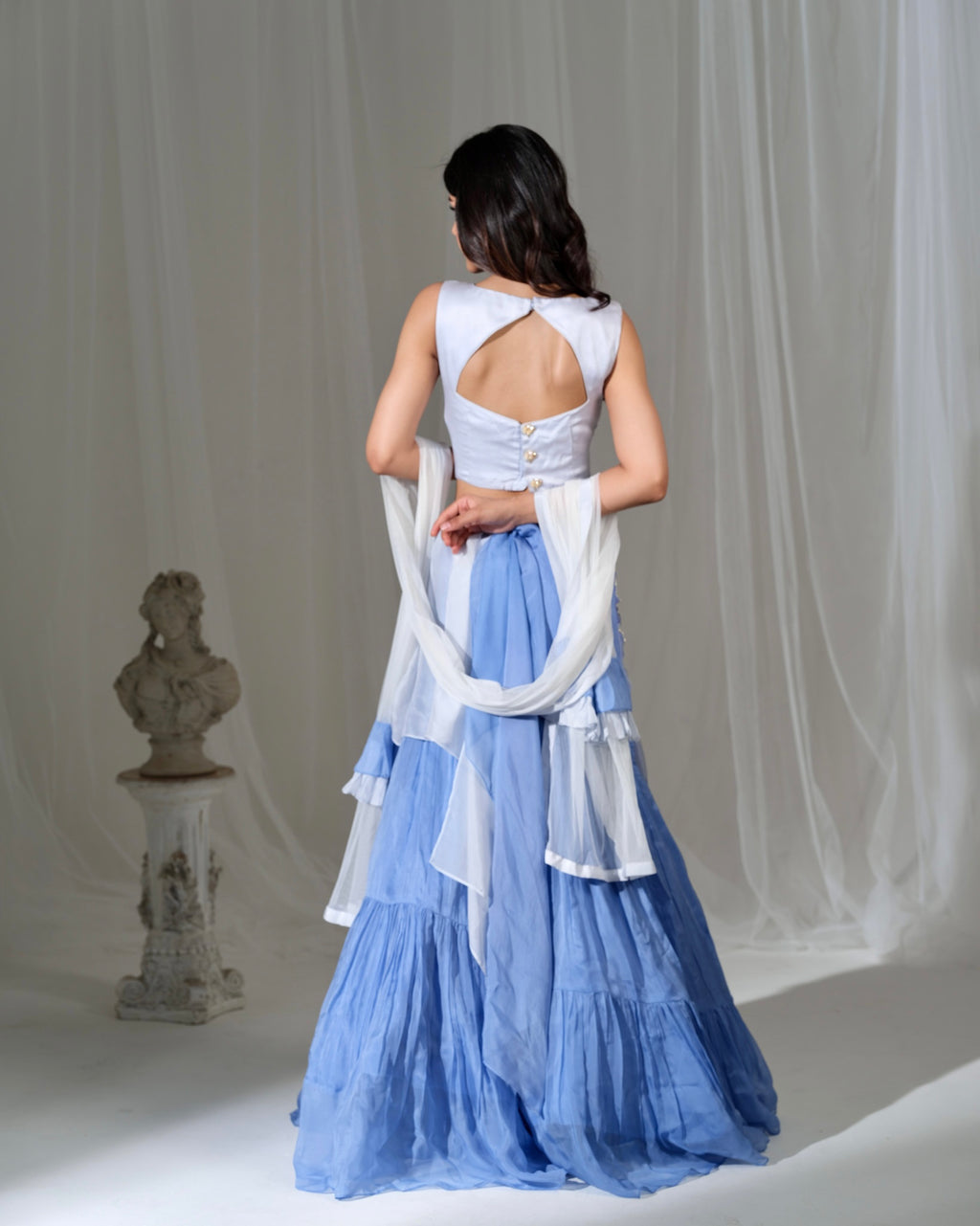 Woman wearing a white top and blue dress with a sheer overlay against a neutral background