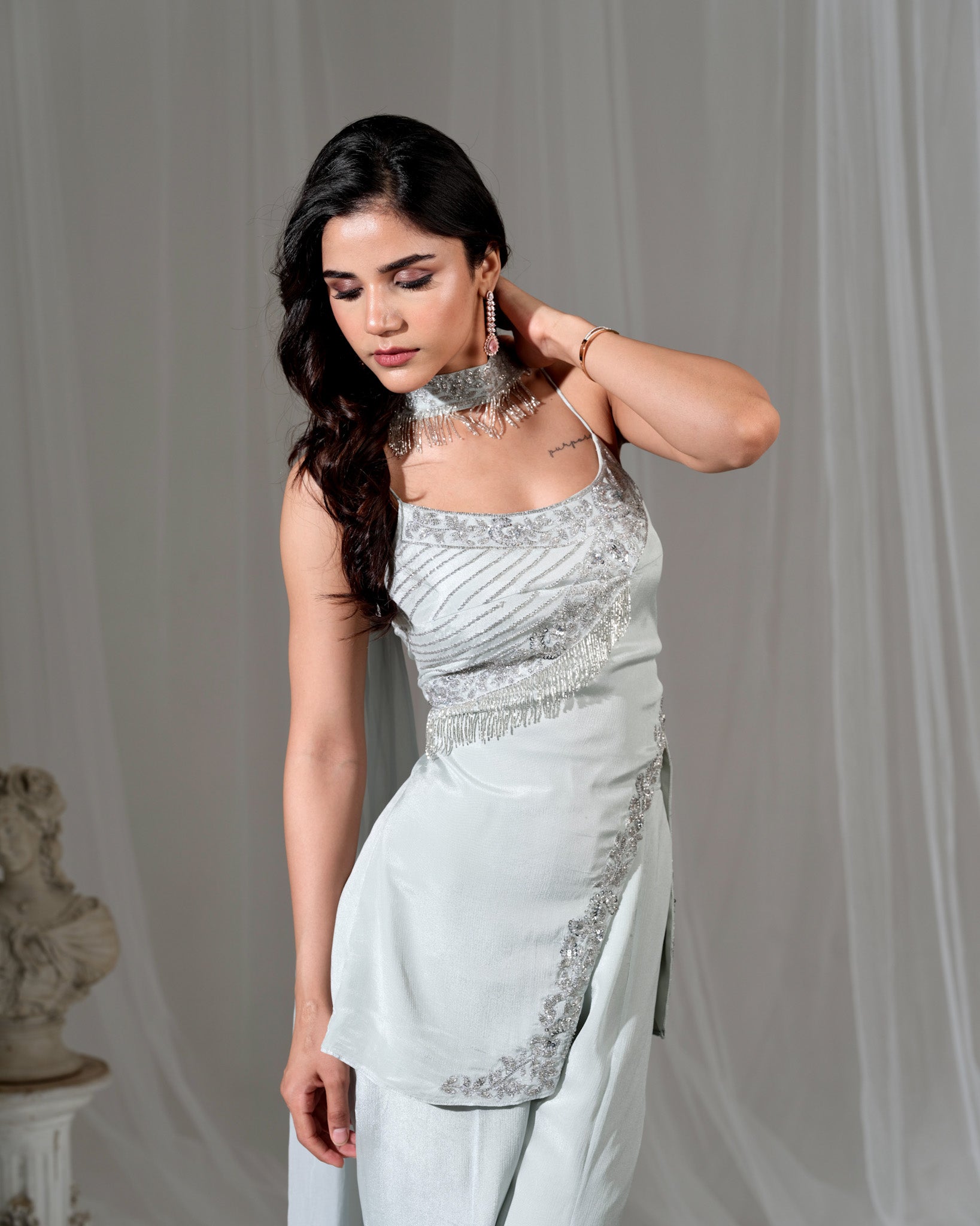 Woman wearing a silver and white dress with intricate detailing against a plain background