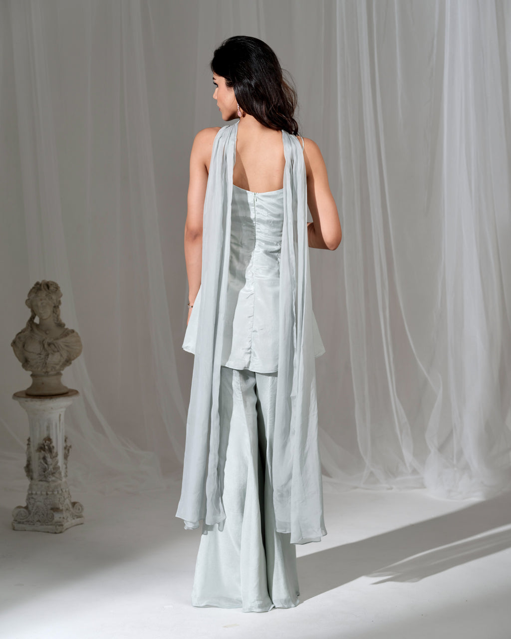 Woman wearing a light blue outfit with a draped fabric against a neutral background