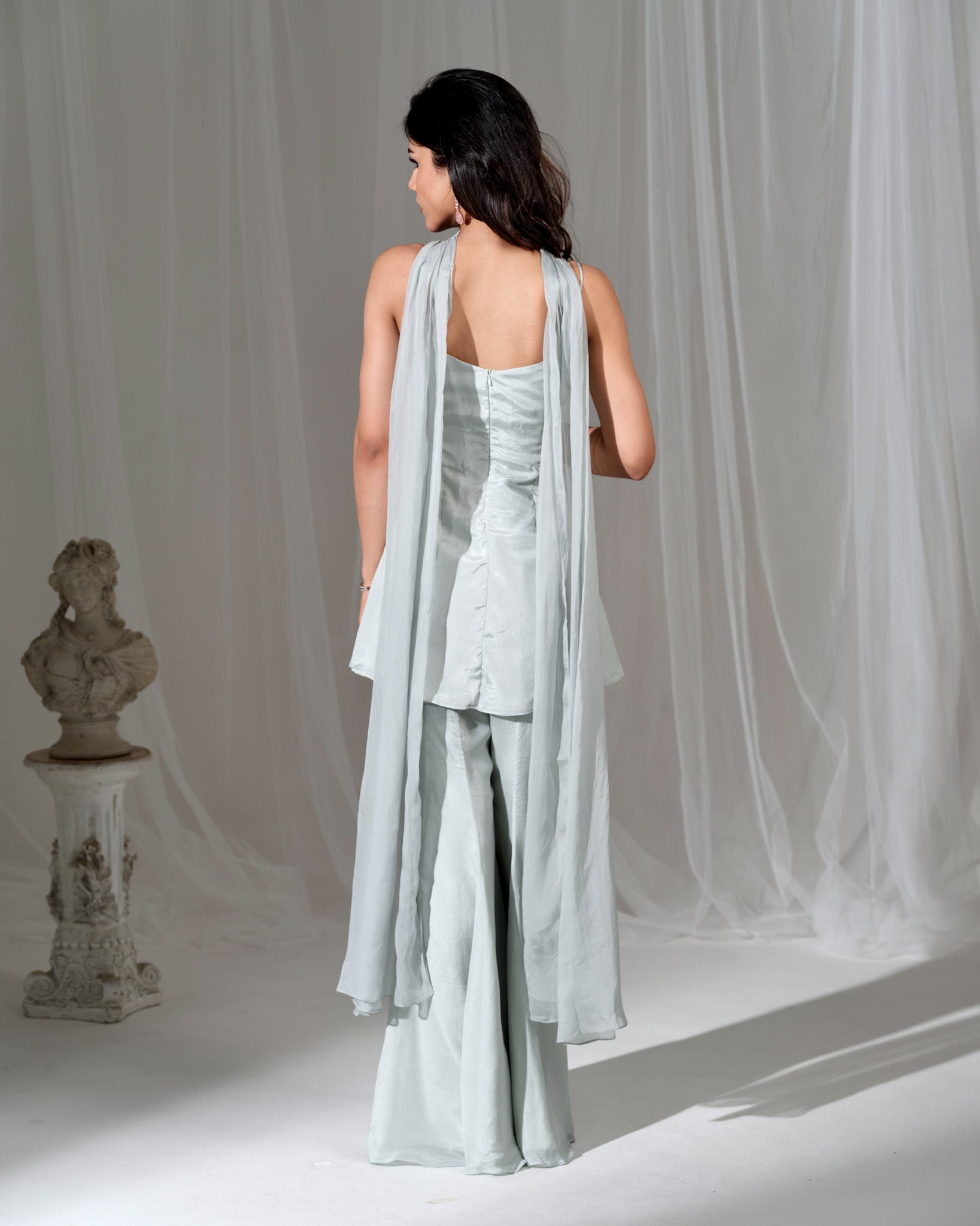 Woman wearing a light blue outfit with a draped fabric against a neutral background