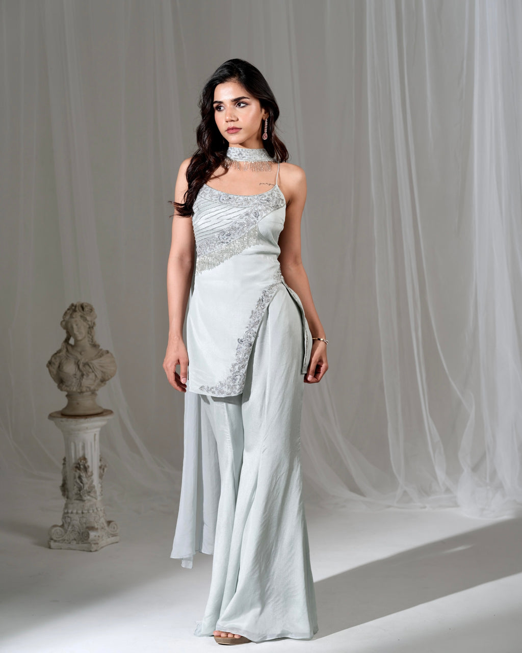 Woman wearing a silver and white evening gown against a gray curtain backdrop.