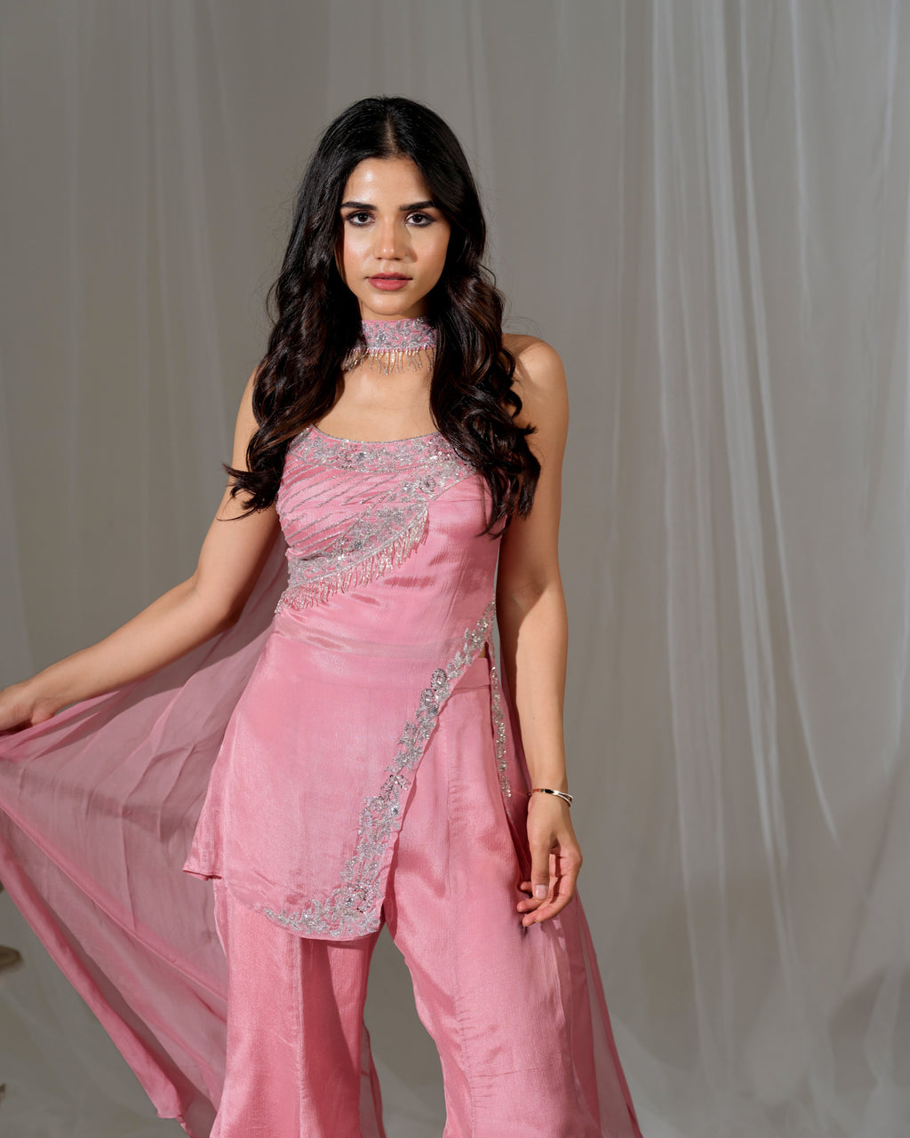 Woman wearing a pink traditional outfit with silver embellishments against a plain background