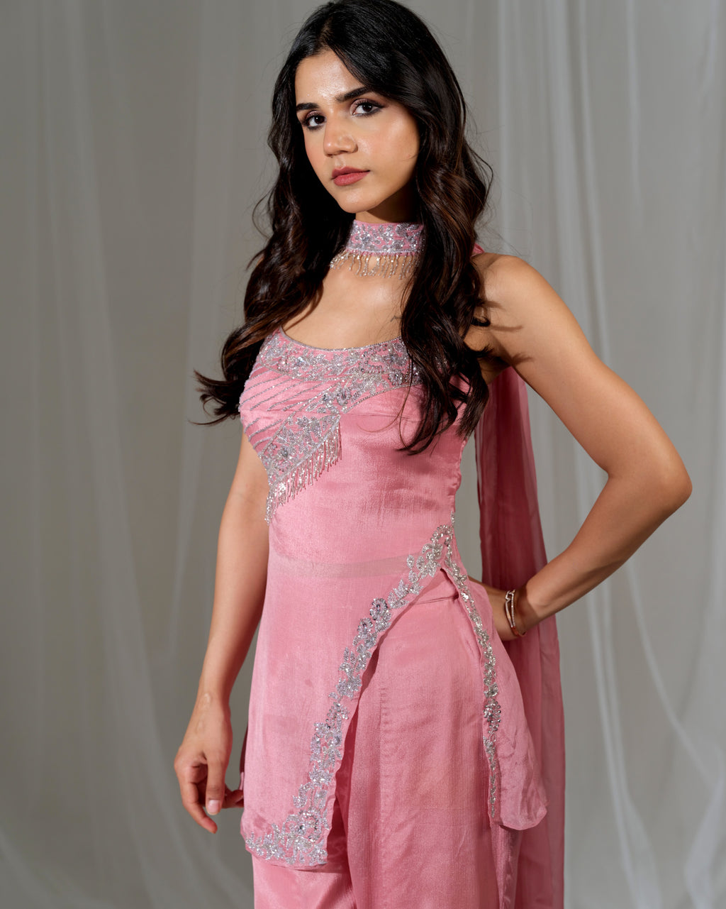 Woman wearing a pink traditional outfit with silver embroidery against a plain background