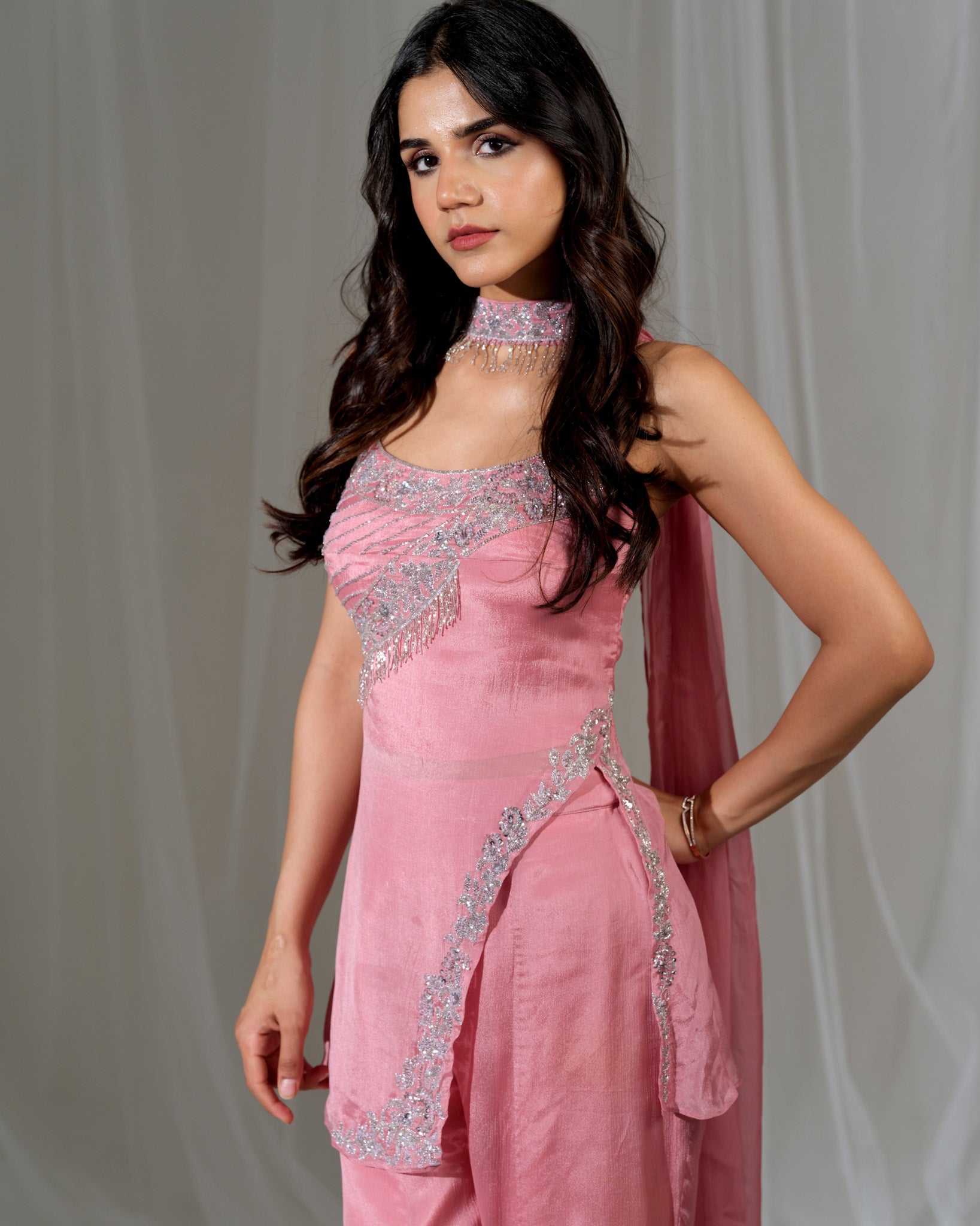 Woman wearing a pink traditional outfit with silver embroidery against a plain background
