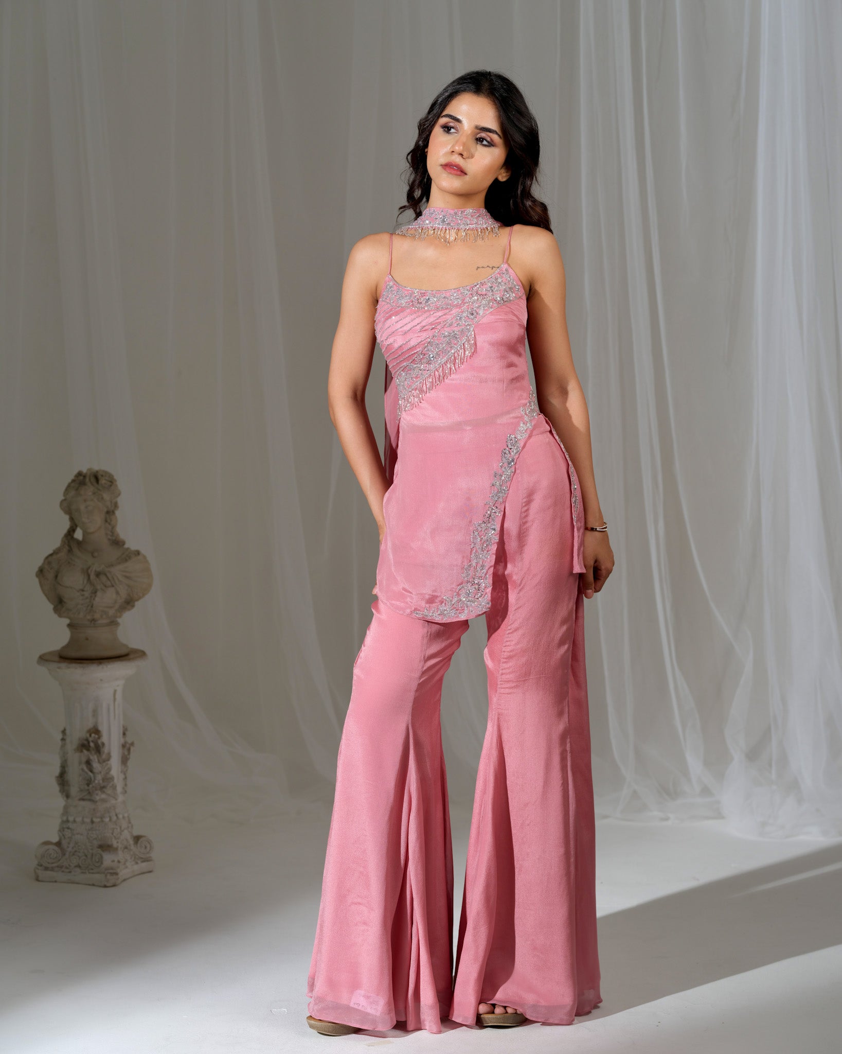 Woman wearing a pink evening gown with silver detailing against a white curtain background
