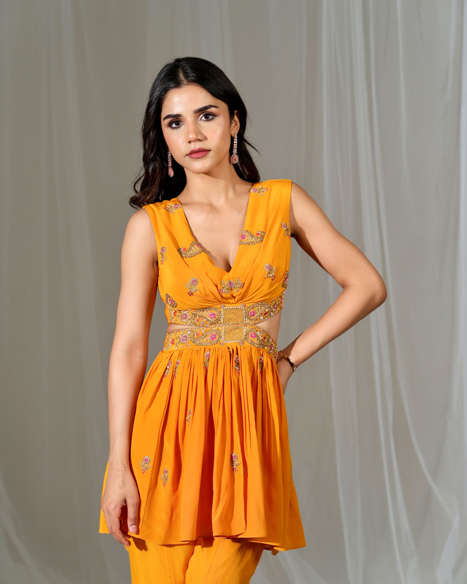 Woman wearing a bright orange dress with floral patterns against a plain background