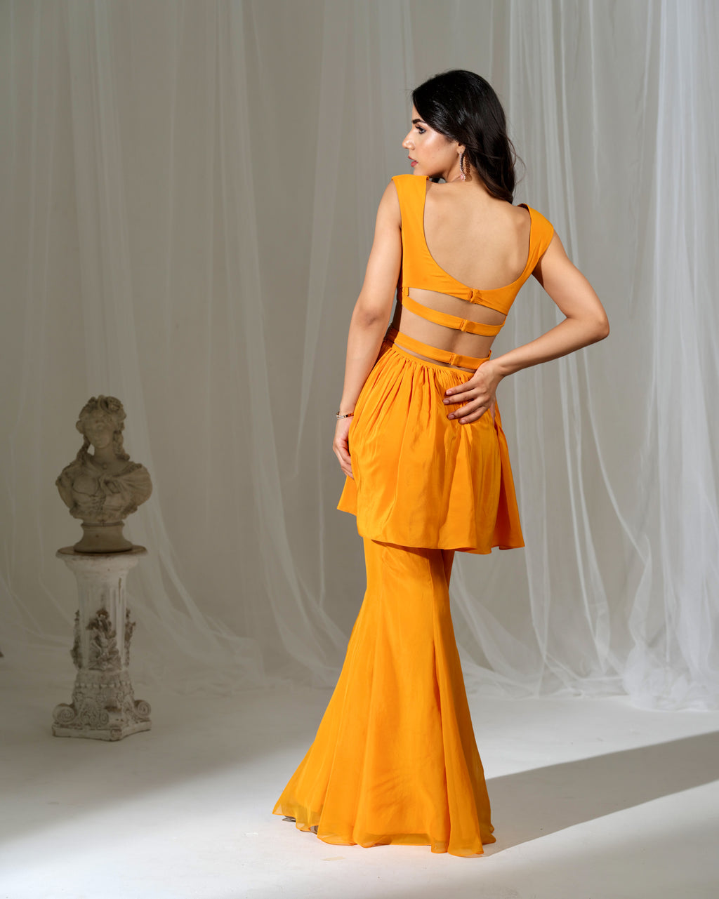 Woman wearing an orange dress with a white curtain background