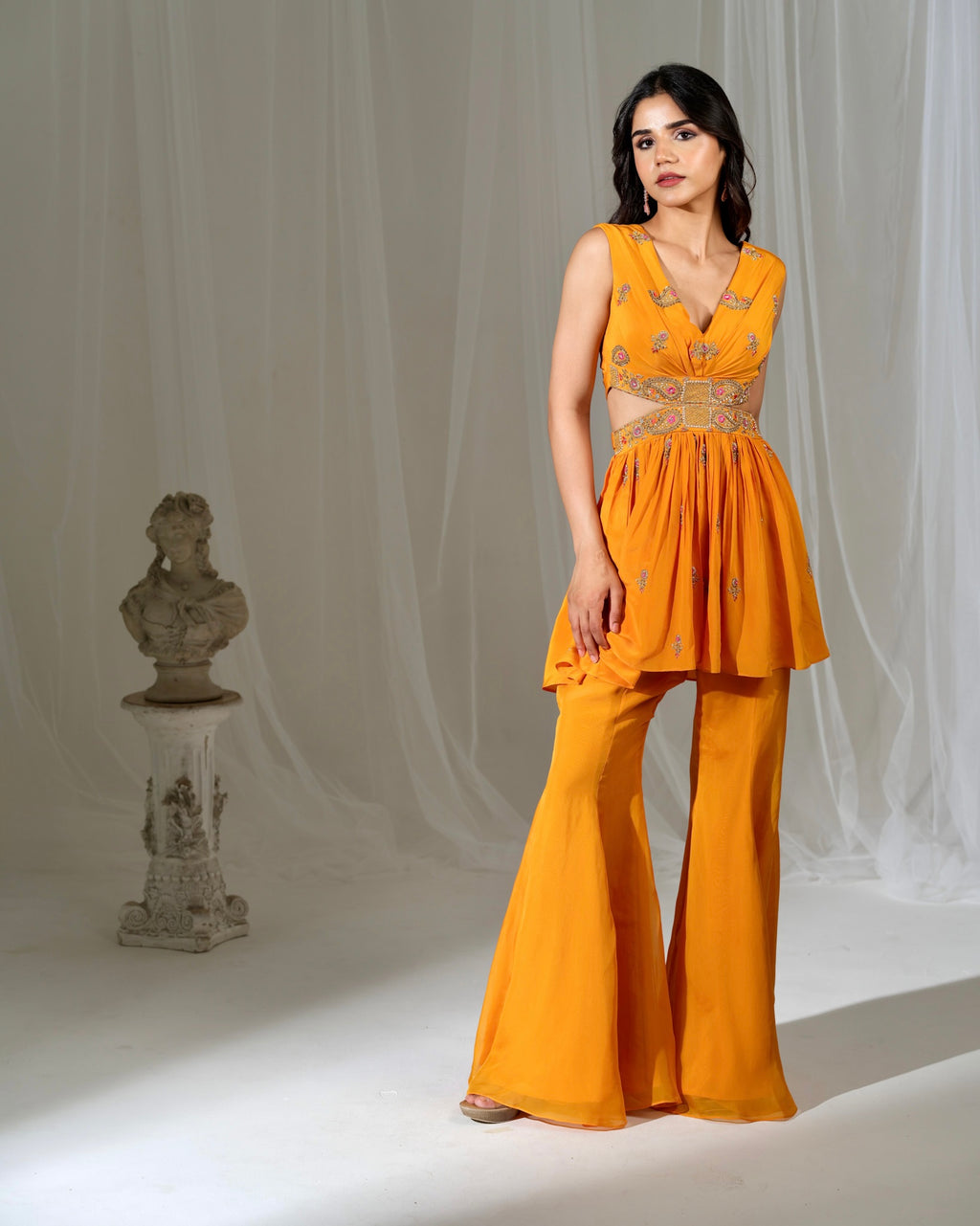 Woman wearing a mustard yellow outfit with a bust and draped fabric in the background