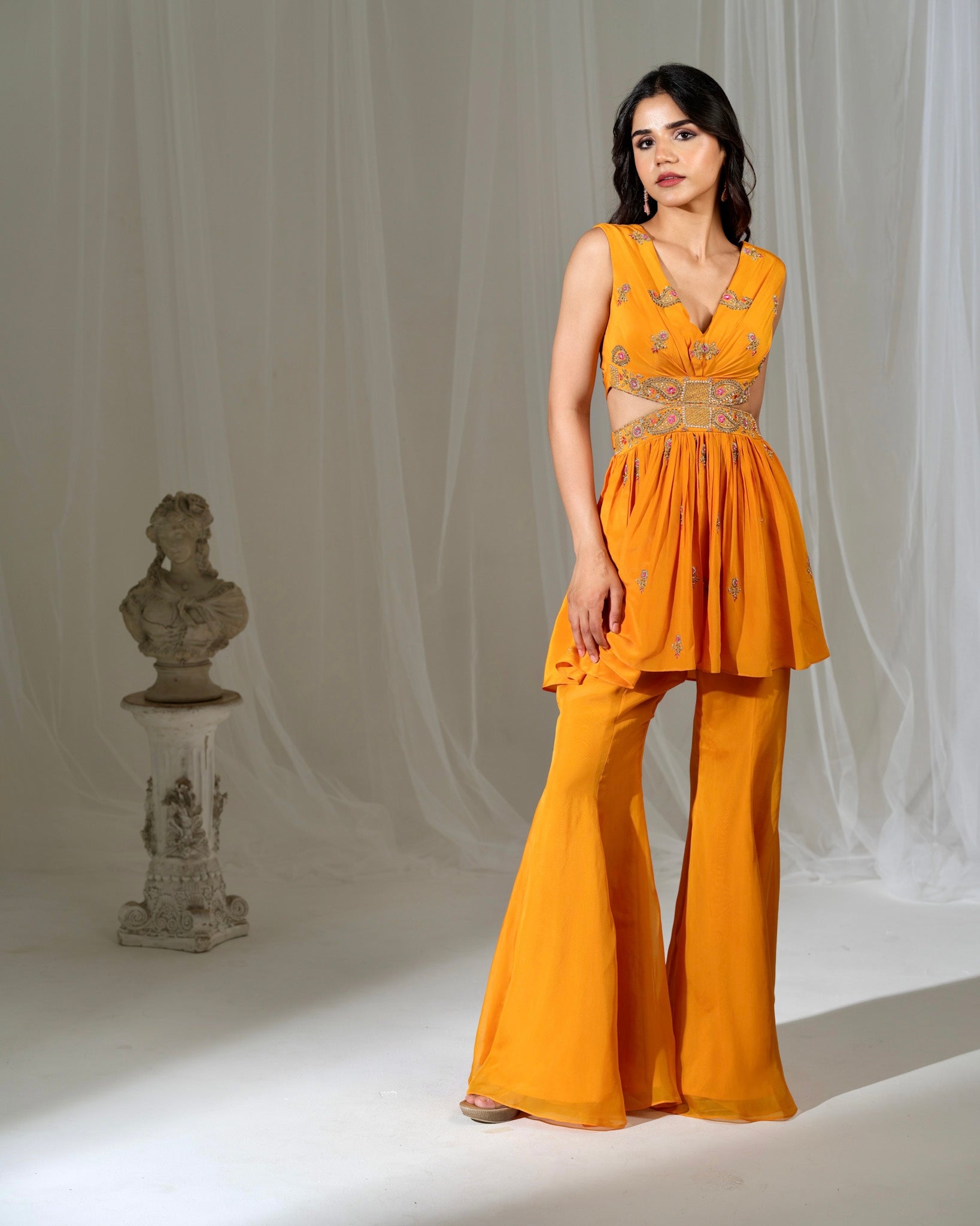 Woman wearing a mustard yellow outfit with a bust and draped fabric in the background