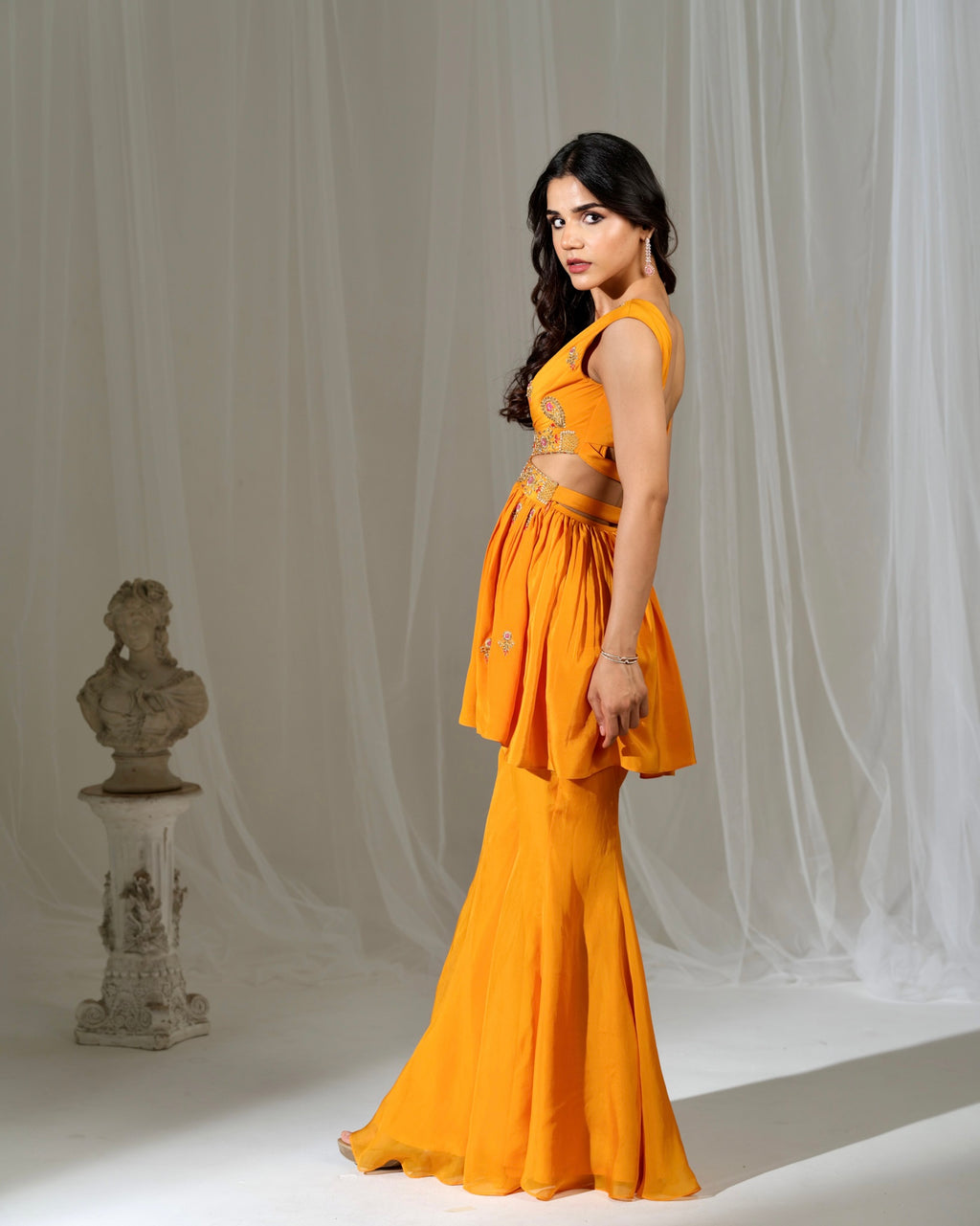 Woman in a mustard yellow outfit standing against a white curtain