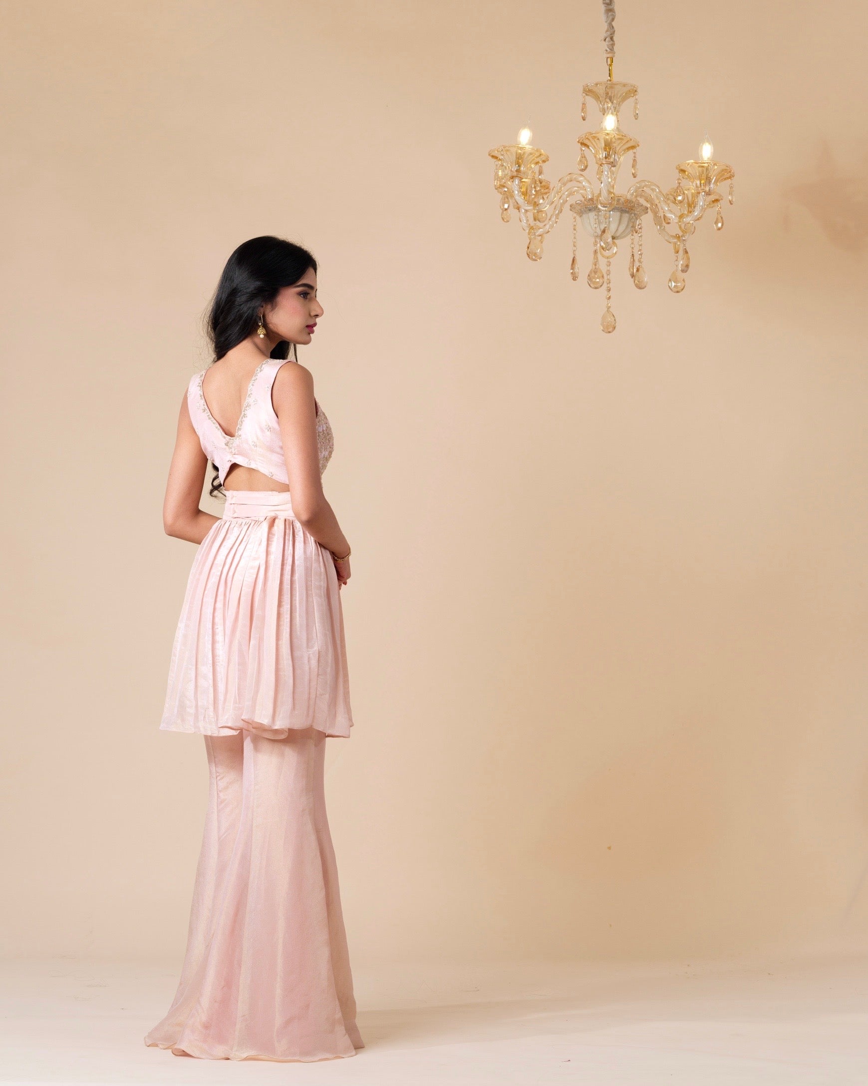 Woman wearing a light pink dress standing in front of a beige wall with a chandelier.