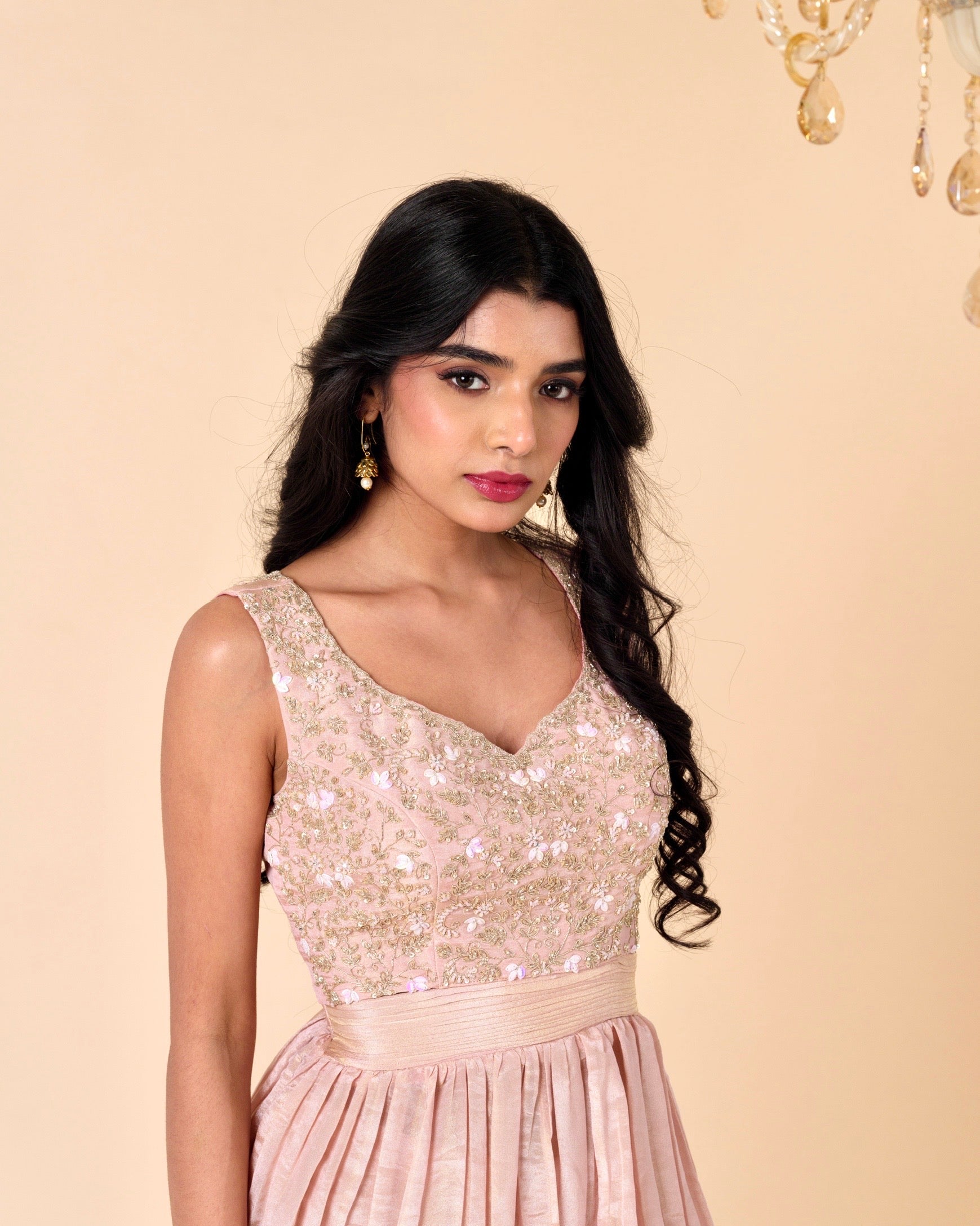 Woman wearing a sparkling top and pink skirt against a beige background