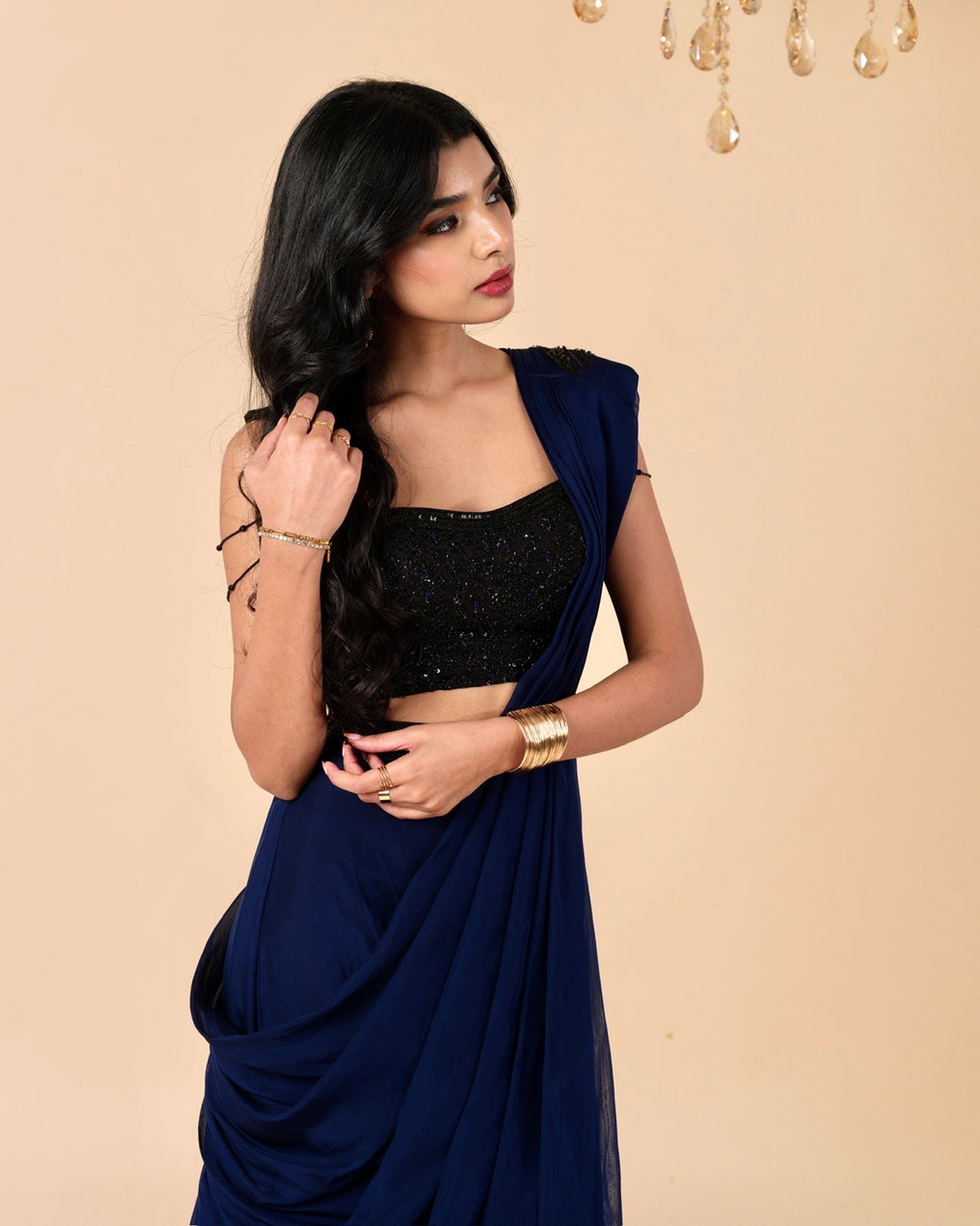 Woman wearing a black blouse and blue saree against a beige background