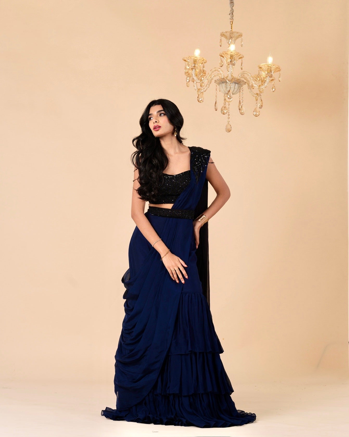 Woman wearing a black and blue saree with a chandelier in the background