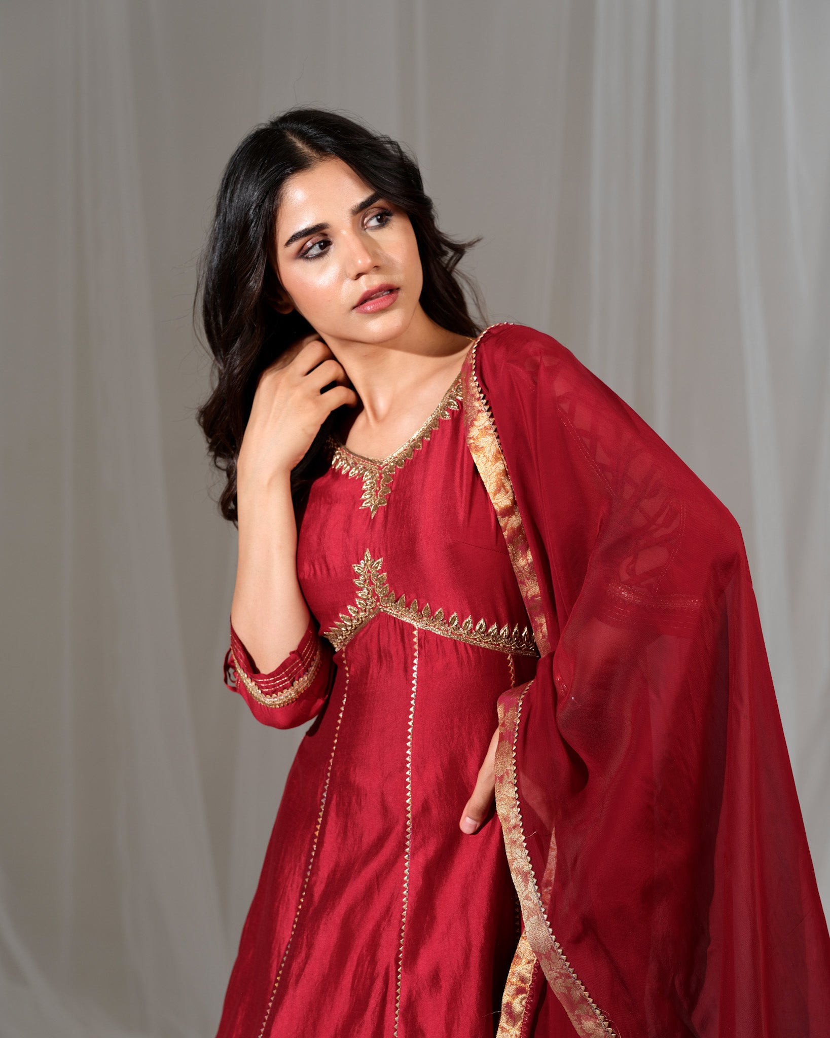 Woman wearing a red traditional outfit with gold embroidery against a plain background
