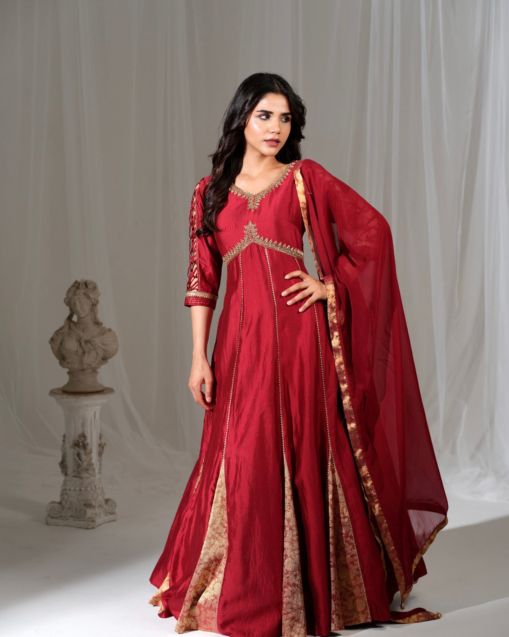 Woman wearing a red traditional outfit with gold details against a plain background