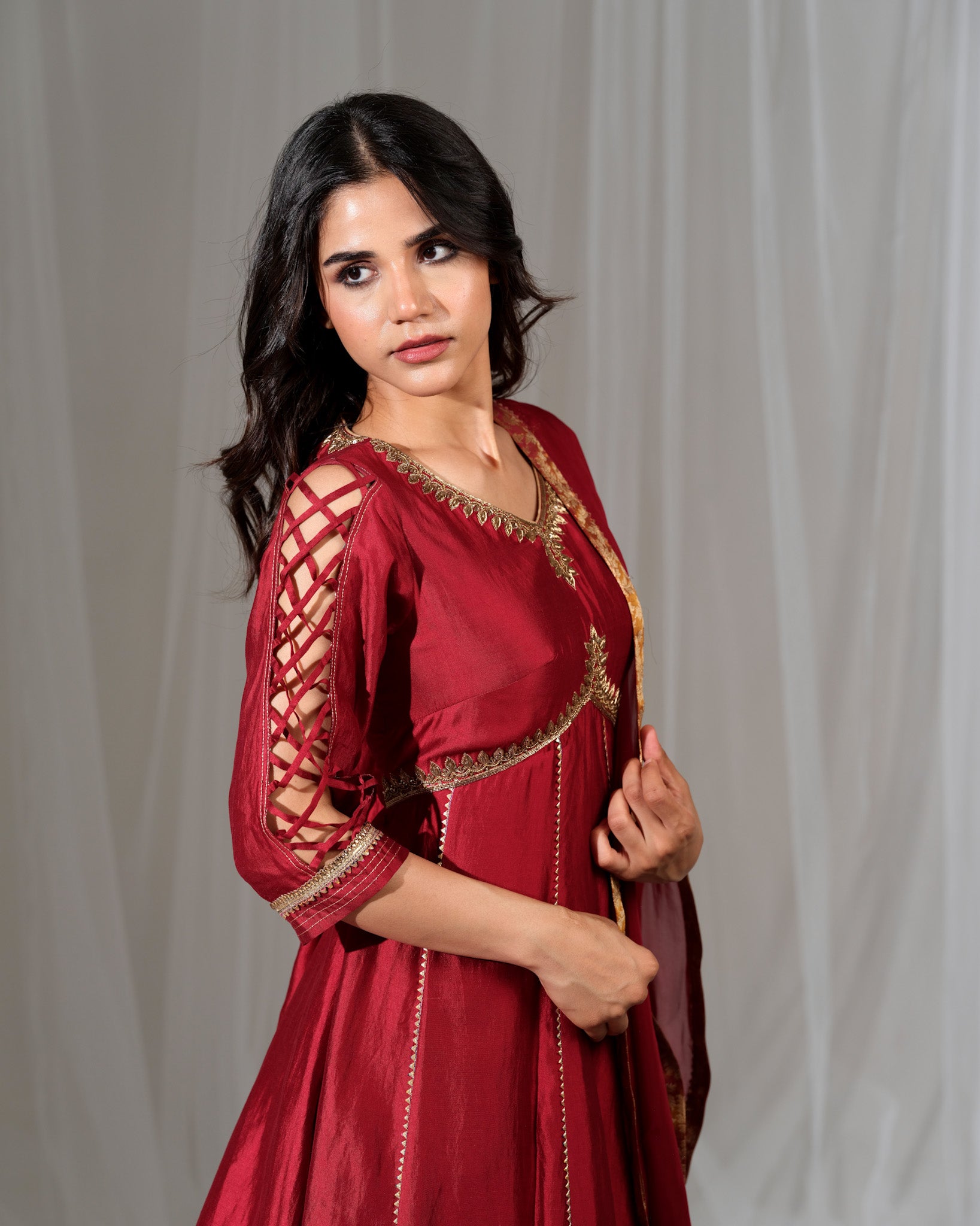 Woman wearing a red traditional outfit with gold embroidery against a plain background