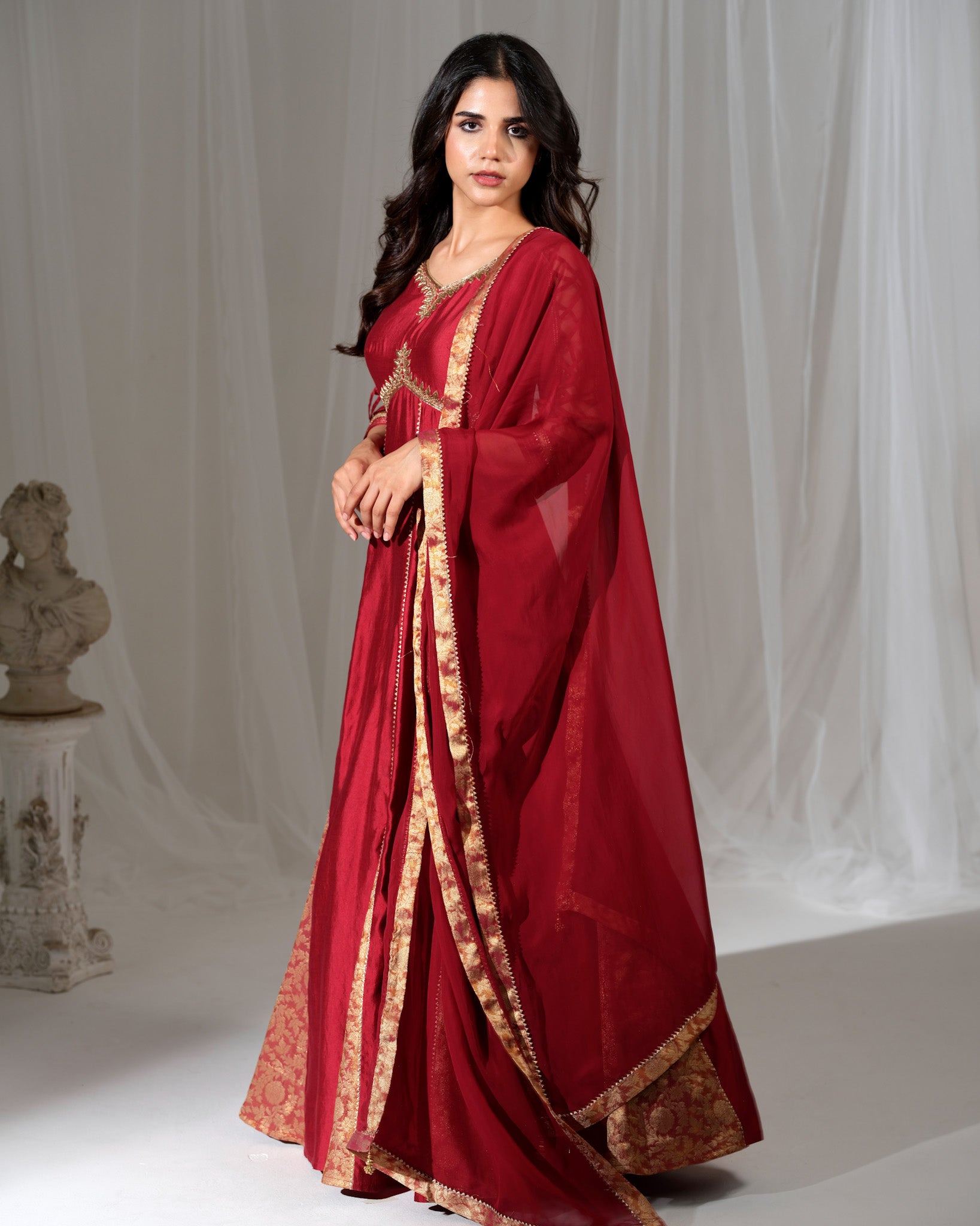 Woman wearing a red traditional outfit with gold accents against a neutral background
