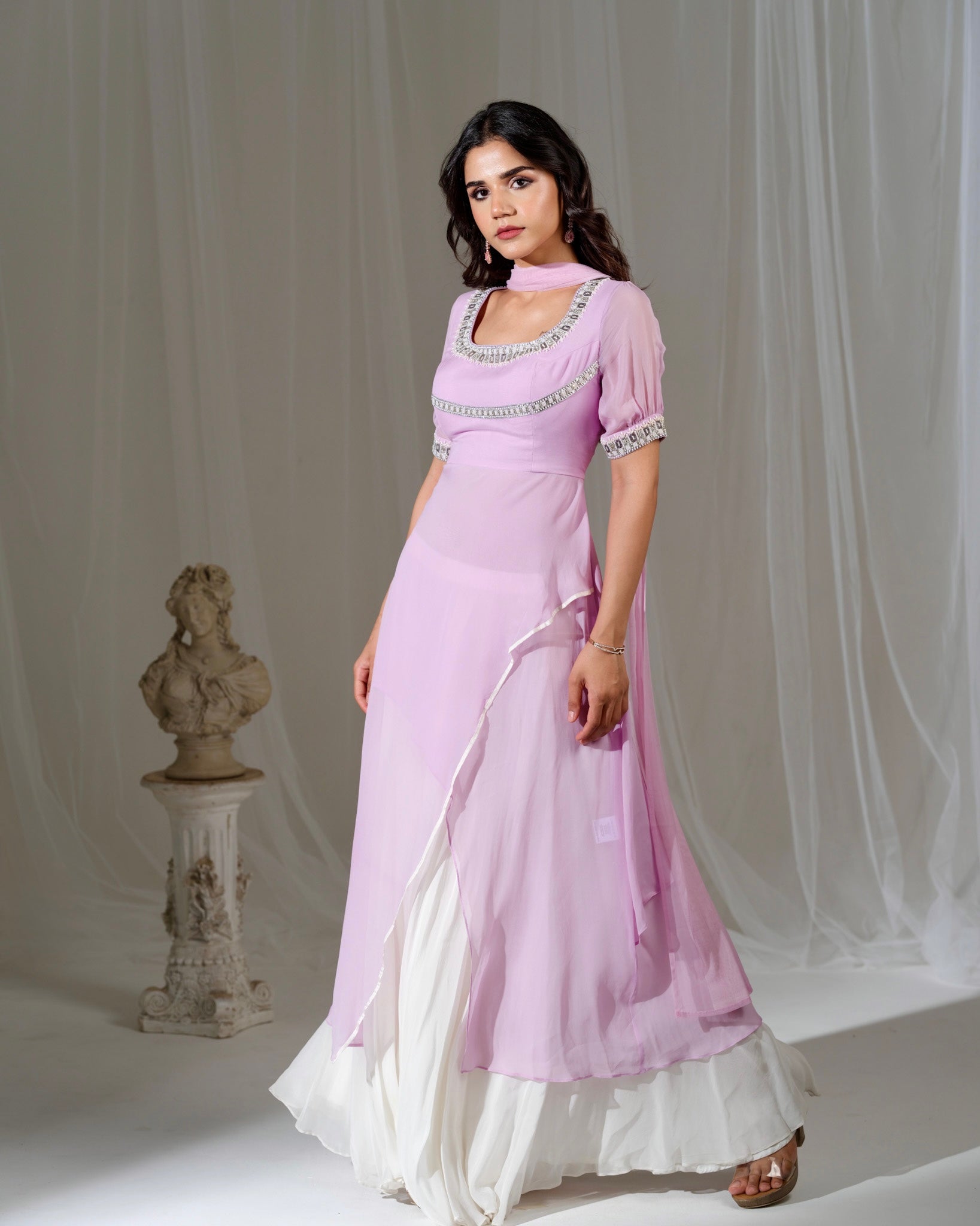 Woman in a pink saree with white border standing against a plain background