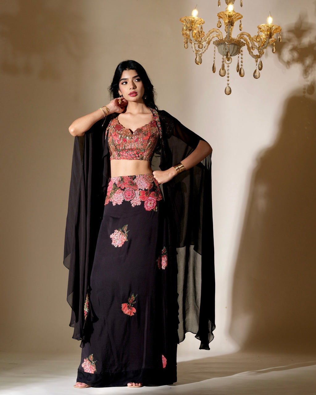 Woman in traditional outfit with floral patterns in a dimly lit room with chandelier.